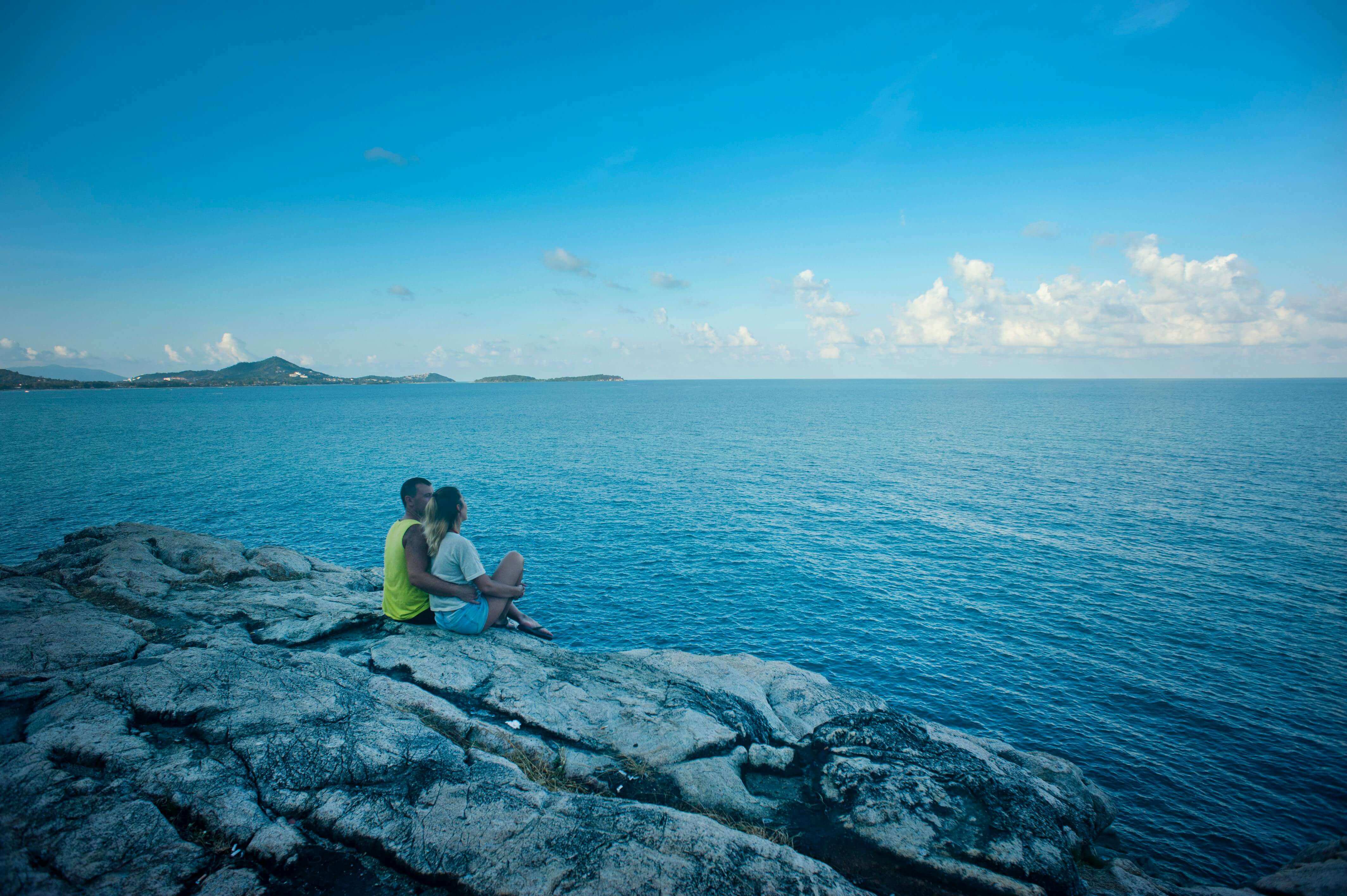 Young couple enjoys a romantic moment on a cliff overlooking the ocean in Tambon Bo Put, Thailand.