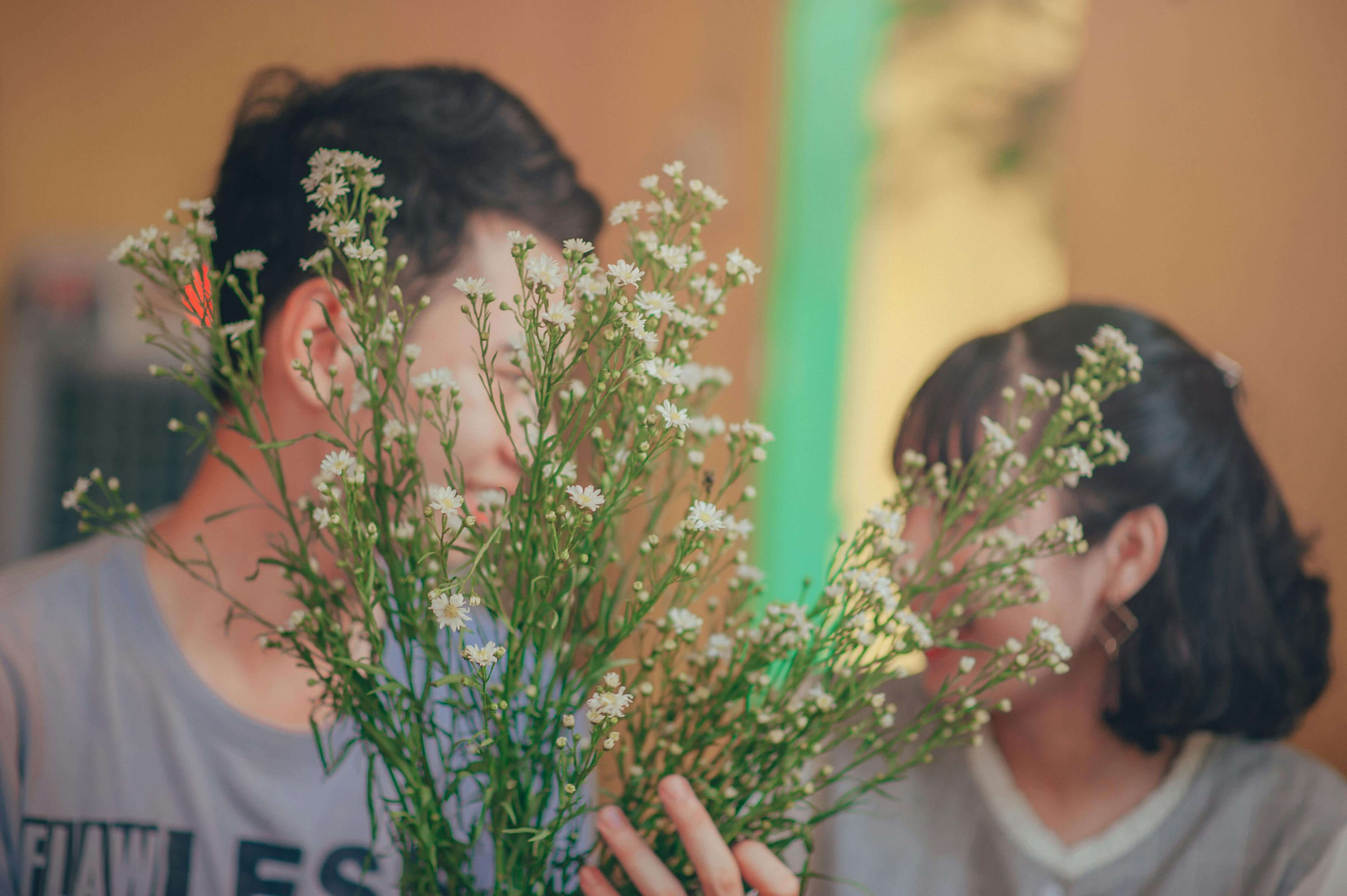 A couple shares a tender moment behind a bouquet of wildflowers, captured in a soft-focus photo.