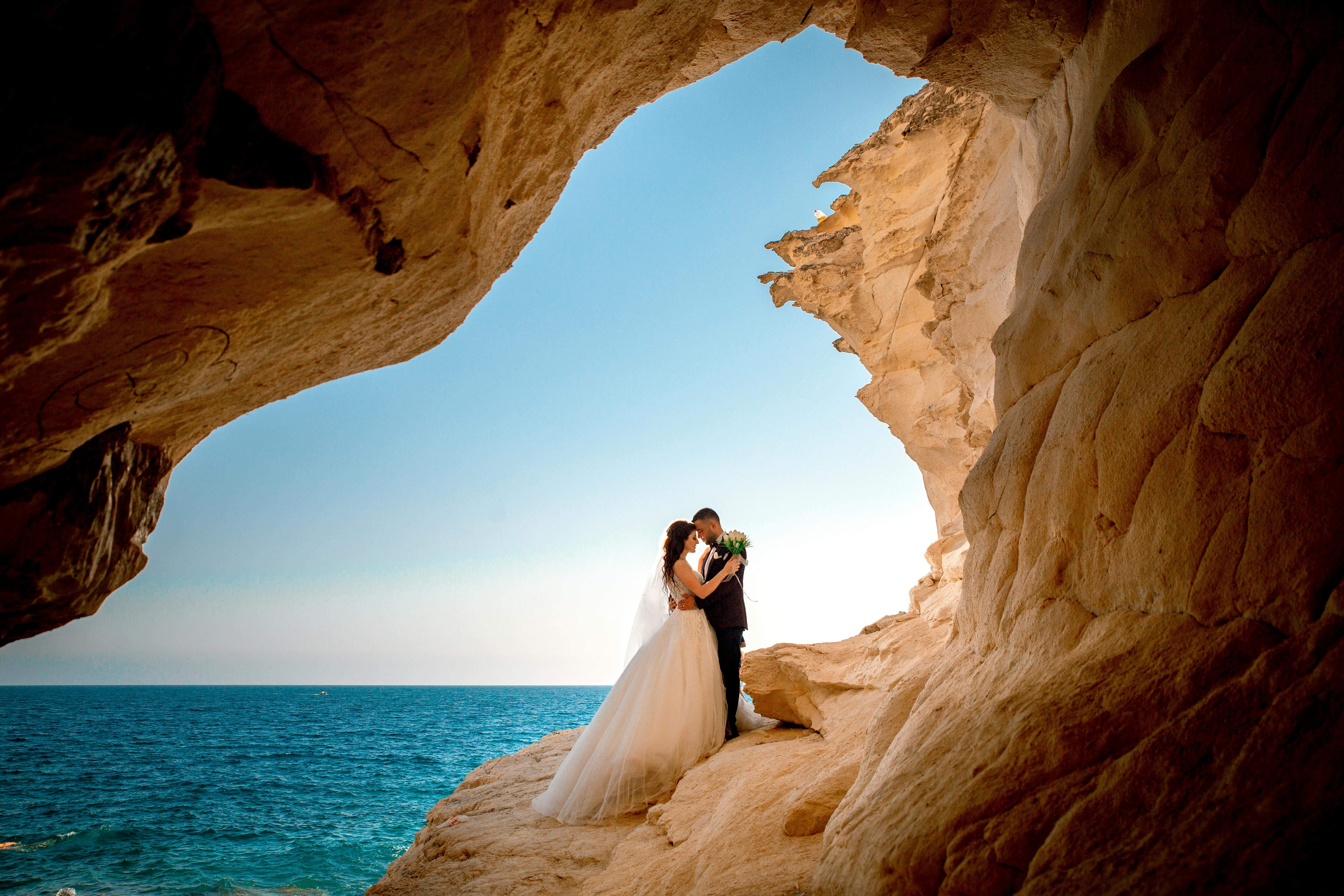 Bride and groom embracing in a rocky coastal setting, celebrating their wedding day with a scenic backdrop.