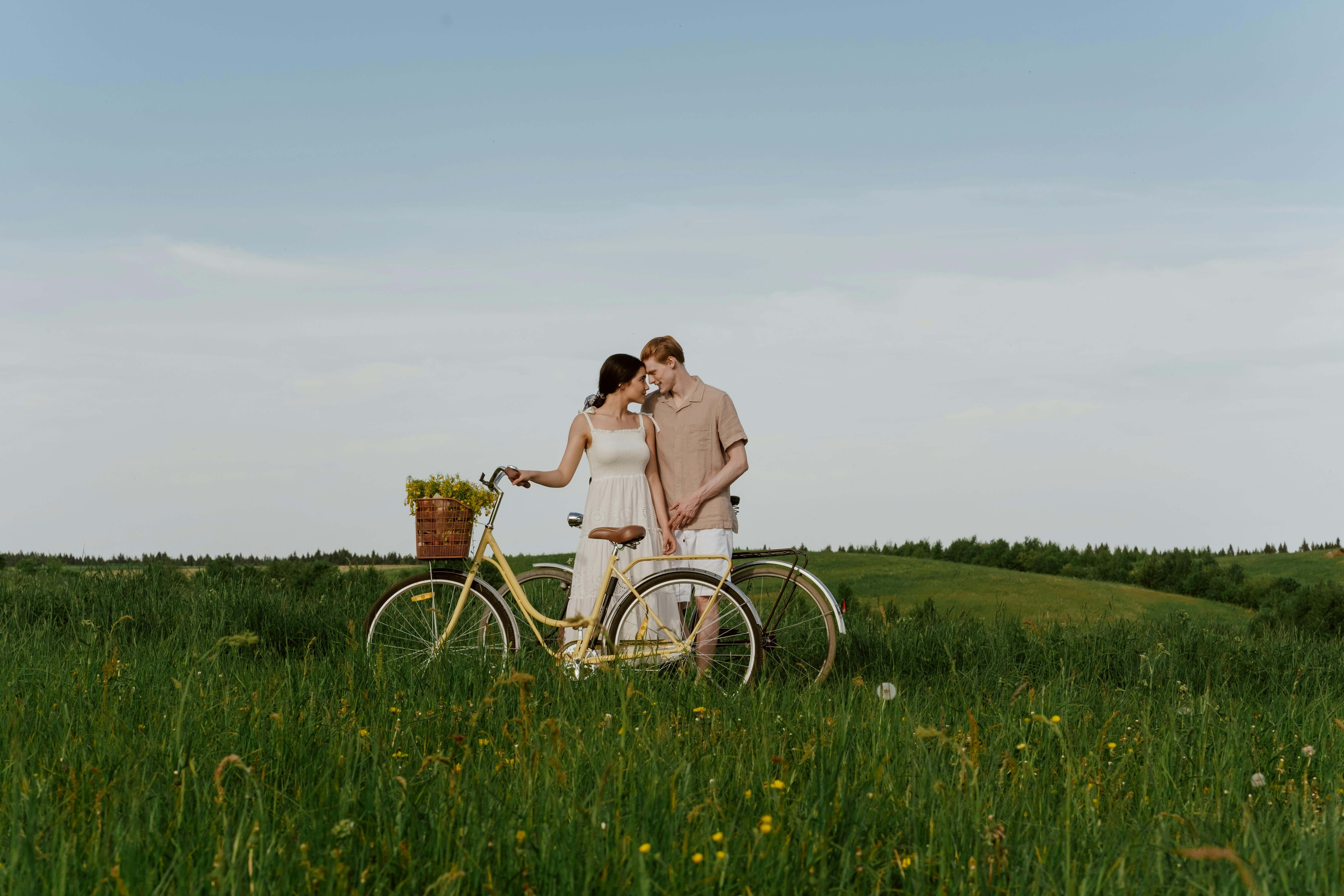Loving couple with a bike in a grassy summer field, enjoying nature outdoors.