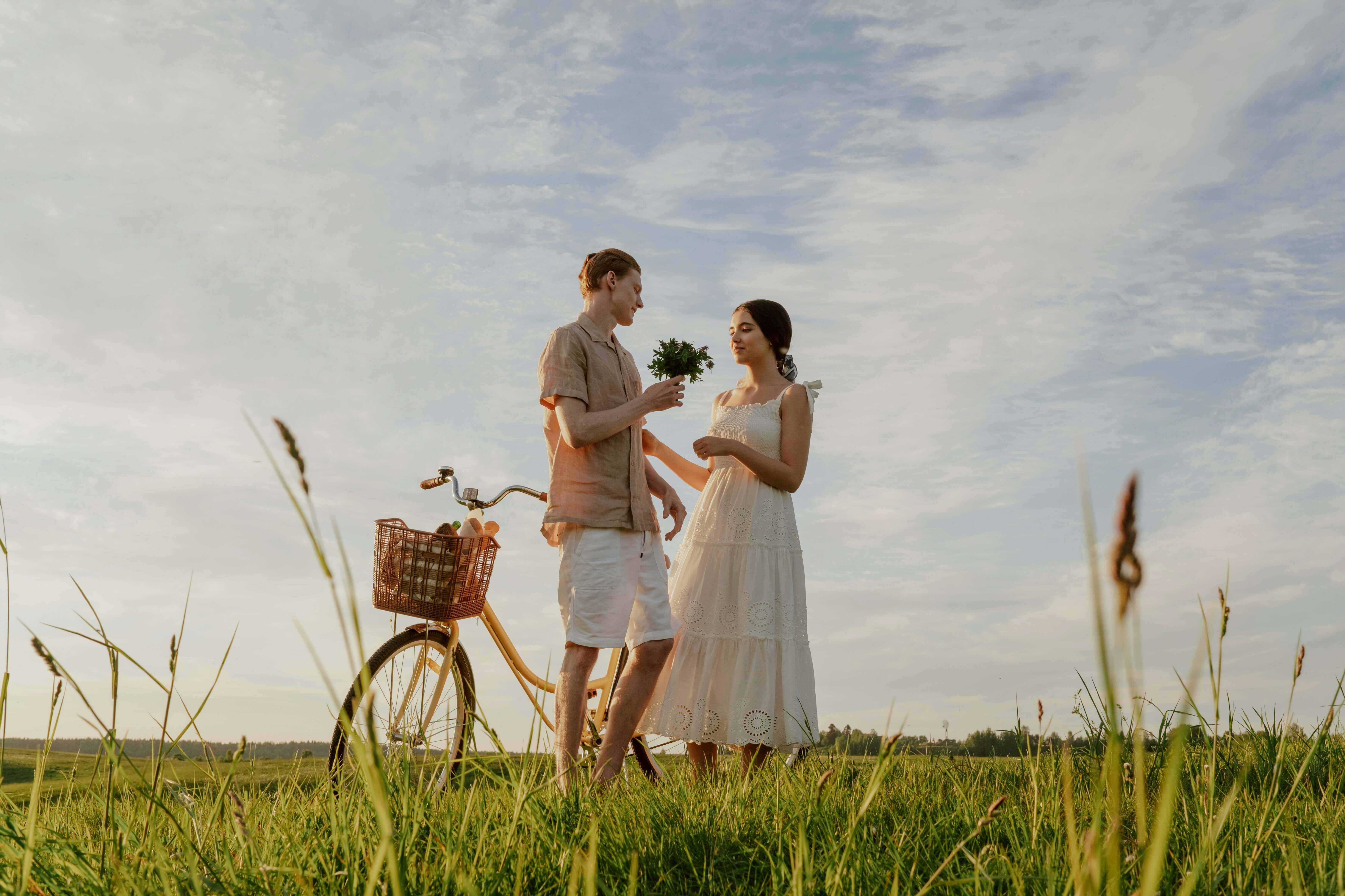 A romantic couple sharing a moment with a bicycle in a sunny field.