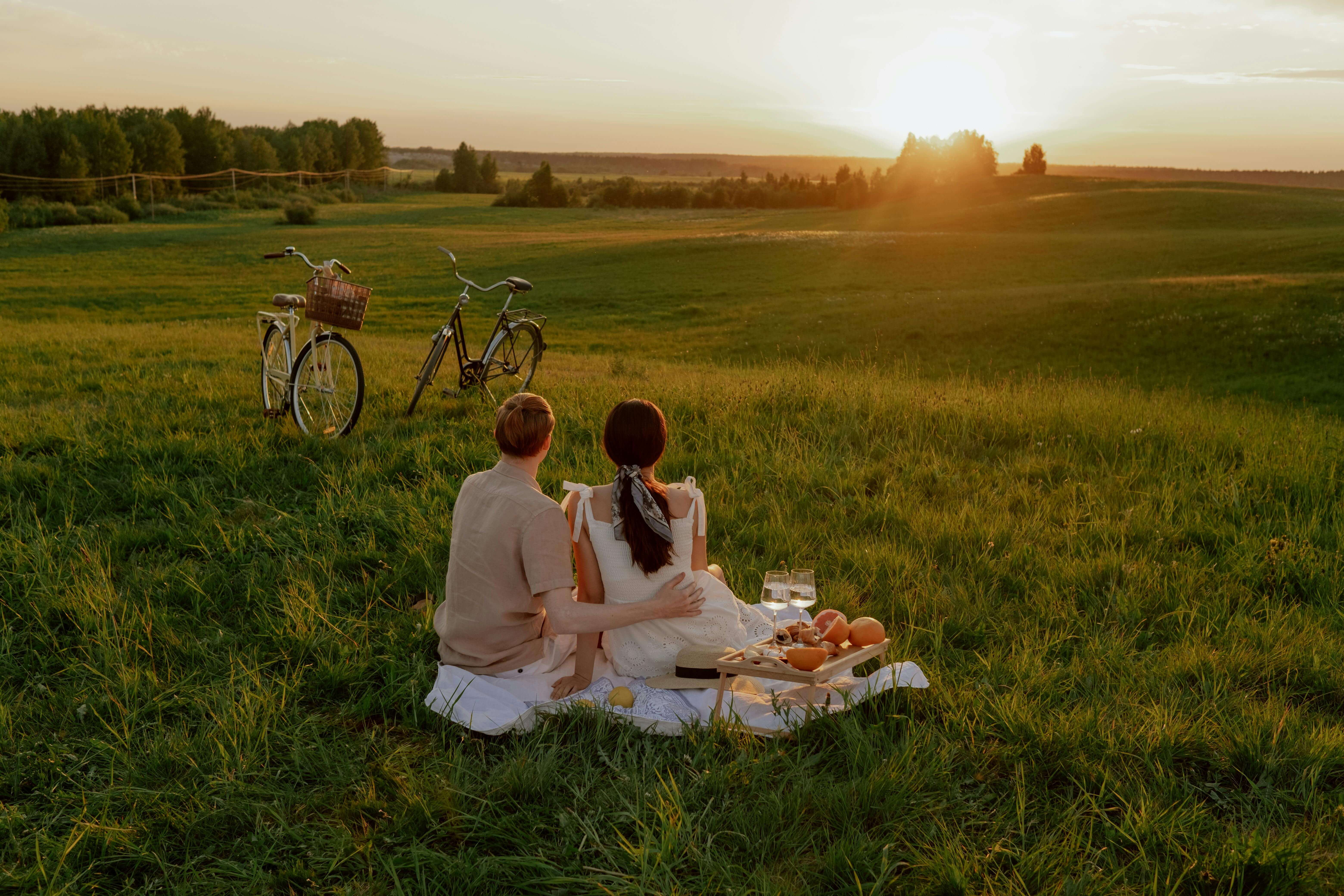 Couple enjoying a romantic picnic with bicycles in a scenic field during sunset.