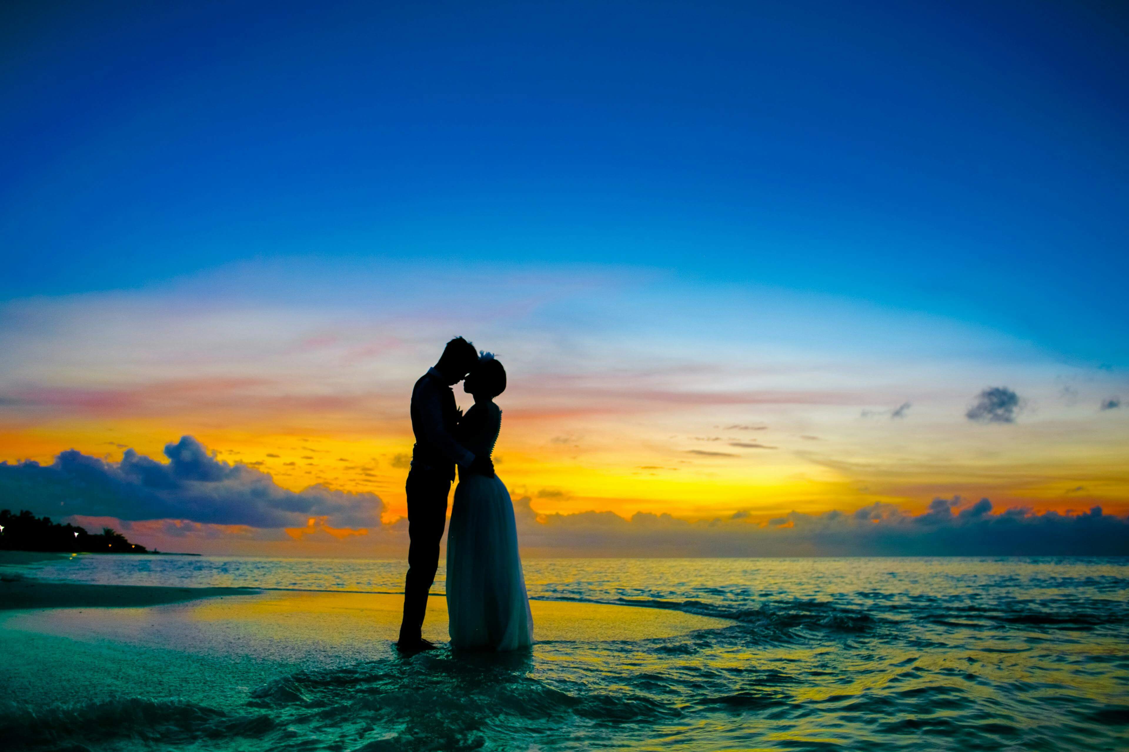 Silhouette of a couple kissing on a tropical beach at sunset, showcasing romance and tranquility.