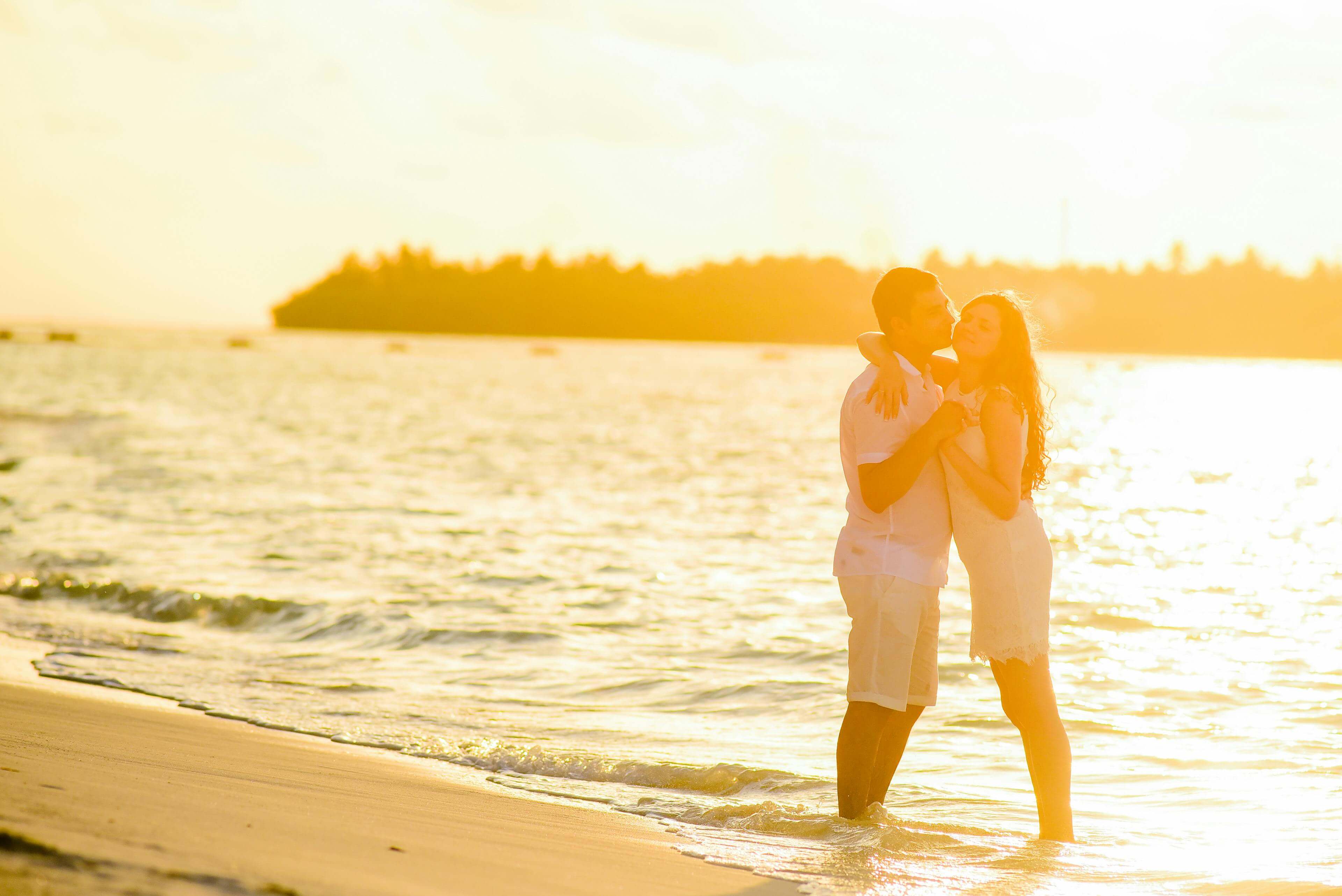 A young couple embracing on a tropical beach during a beautiful sunset, capturing romance and vacation vibes.