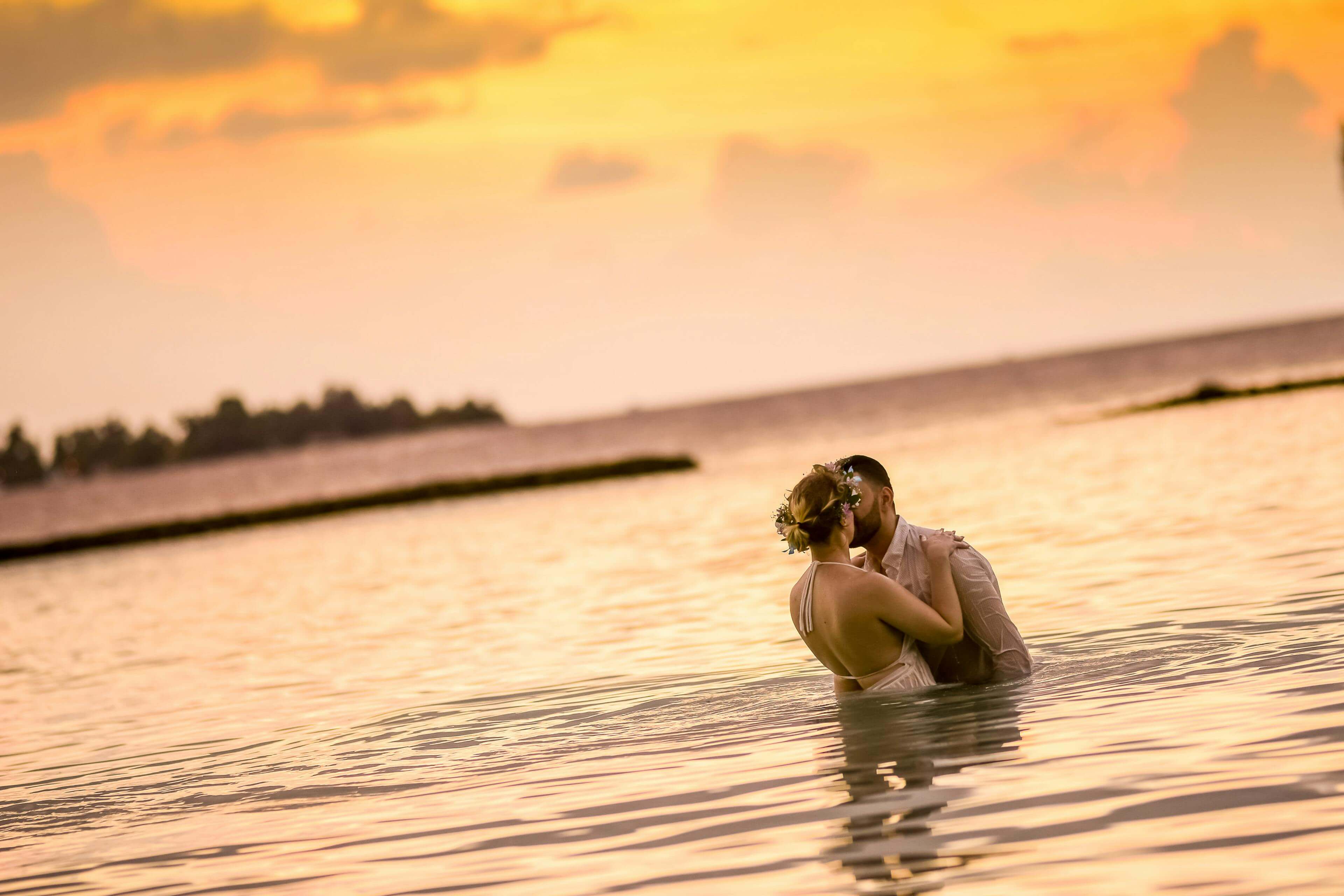 A loving couple kissing in the ocean at sunset, highlighting romantic beach vibes.