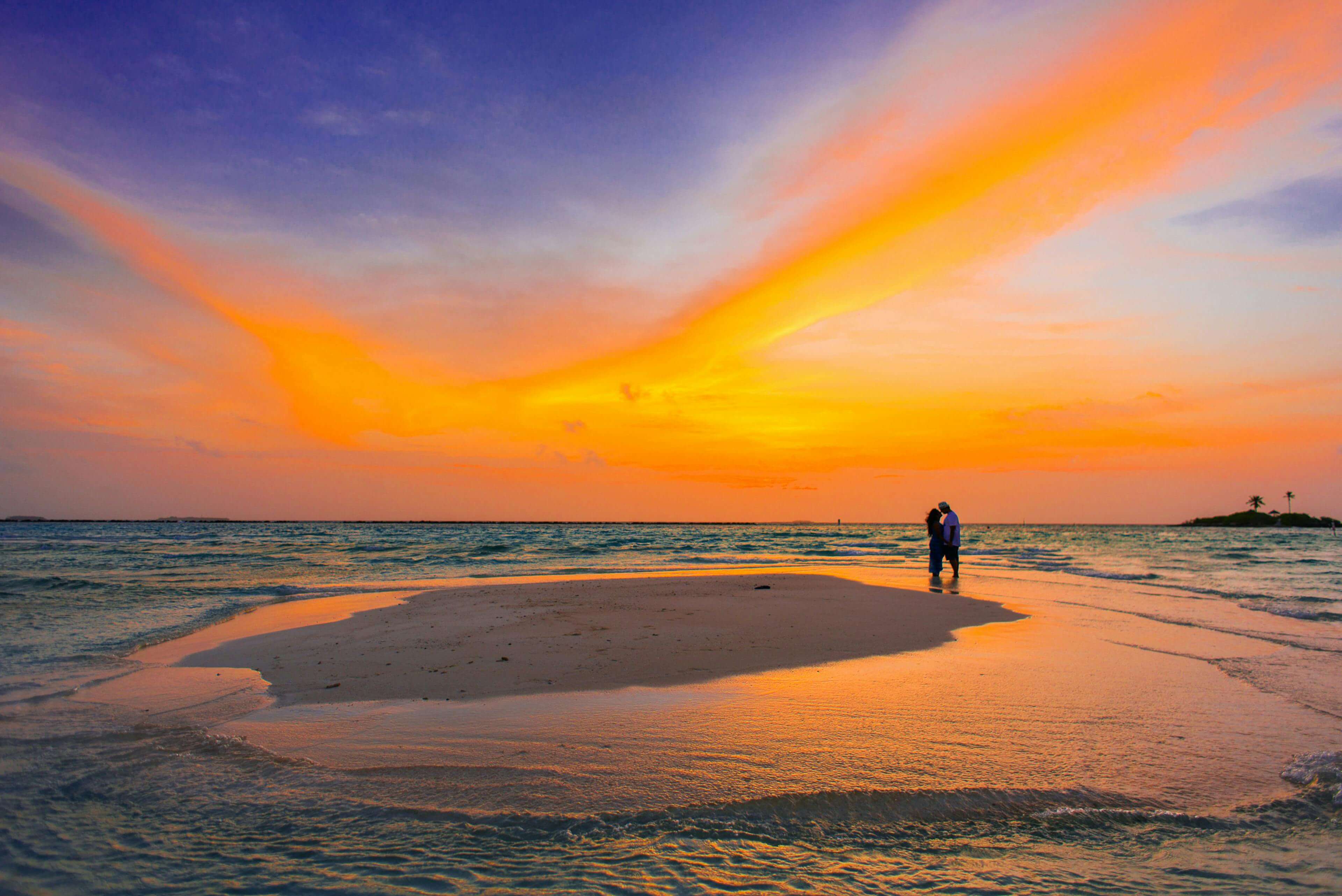 Couple shares a romantic moment on a serene tropical beach at sunset, surrounded by vibrant colors.