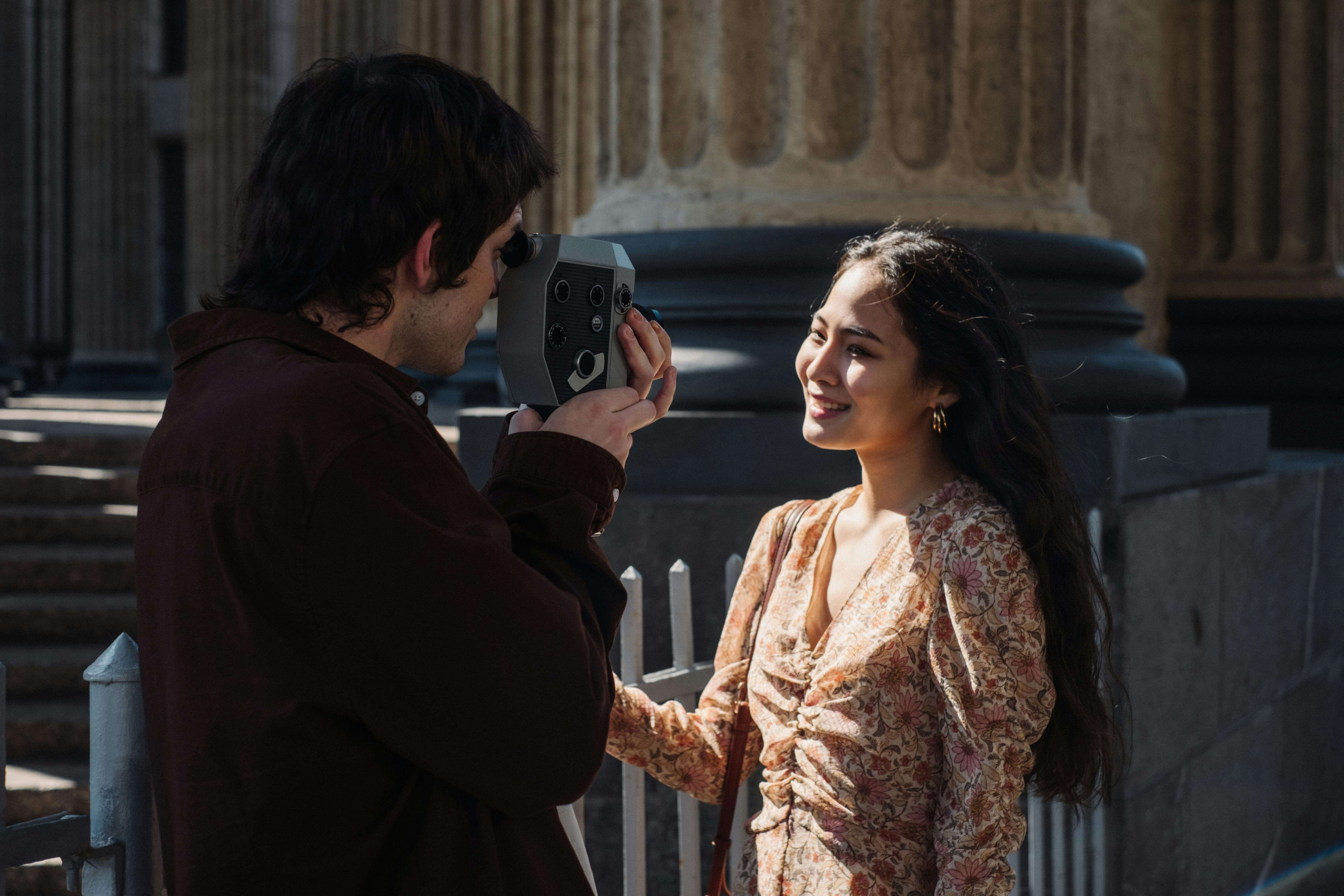 A young couple photographing each other near historic columns in daylight.