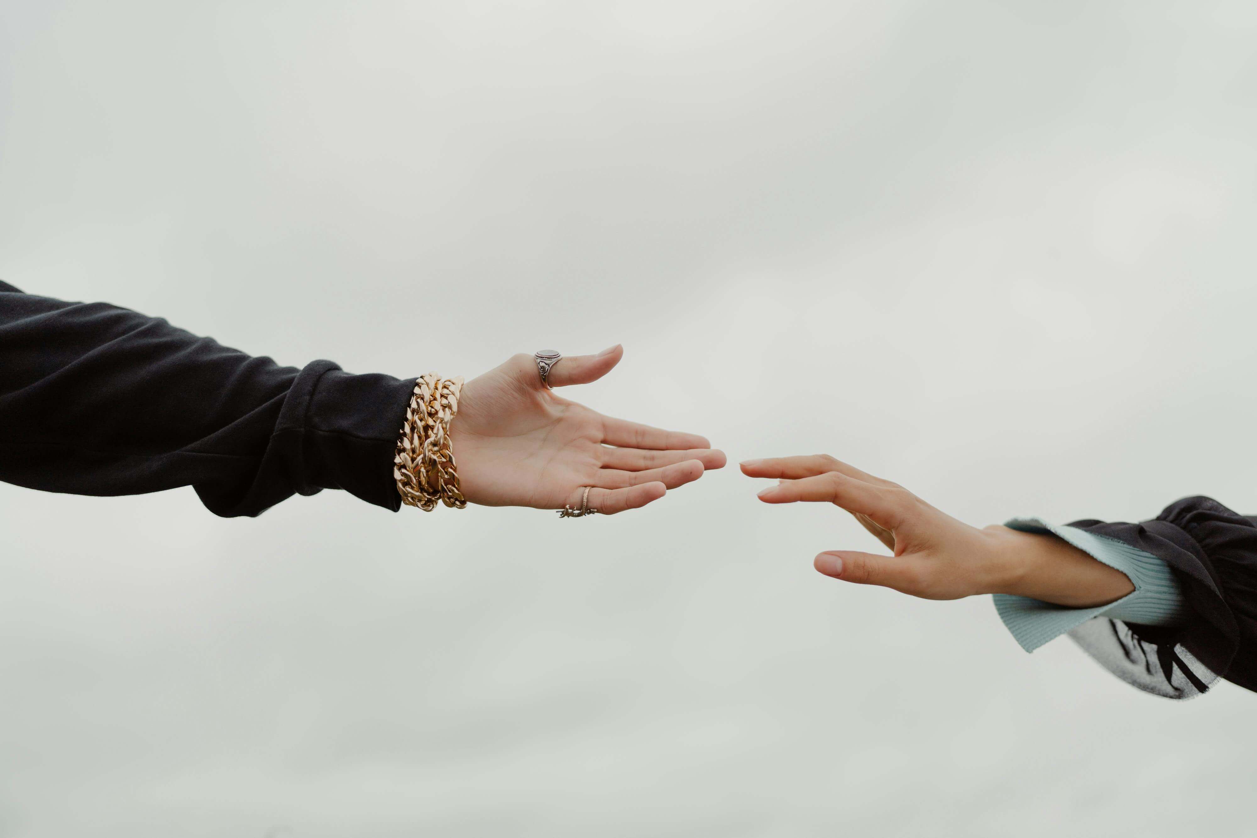 Close-up of two hands reaching for each other under a cloudy sky, symbolizing connection.