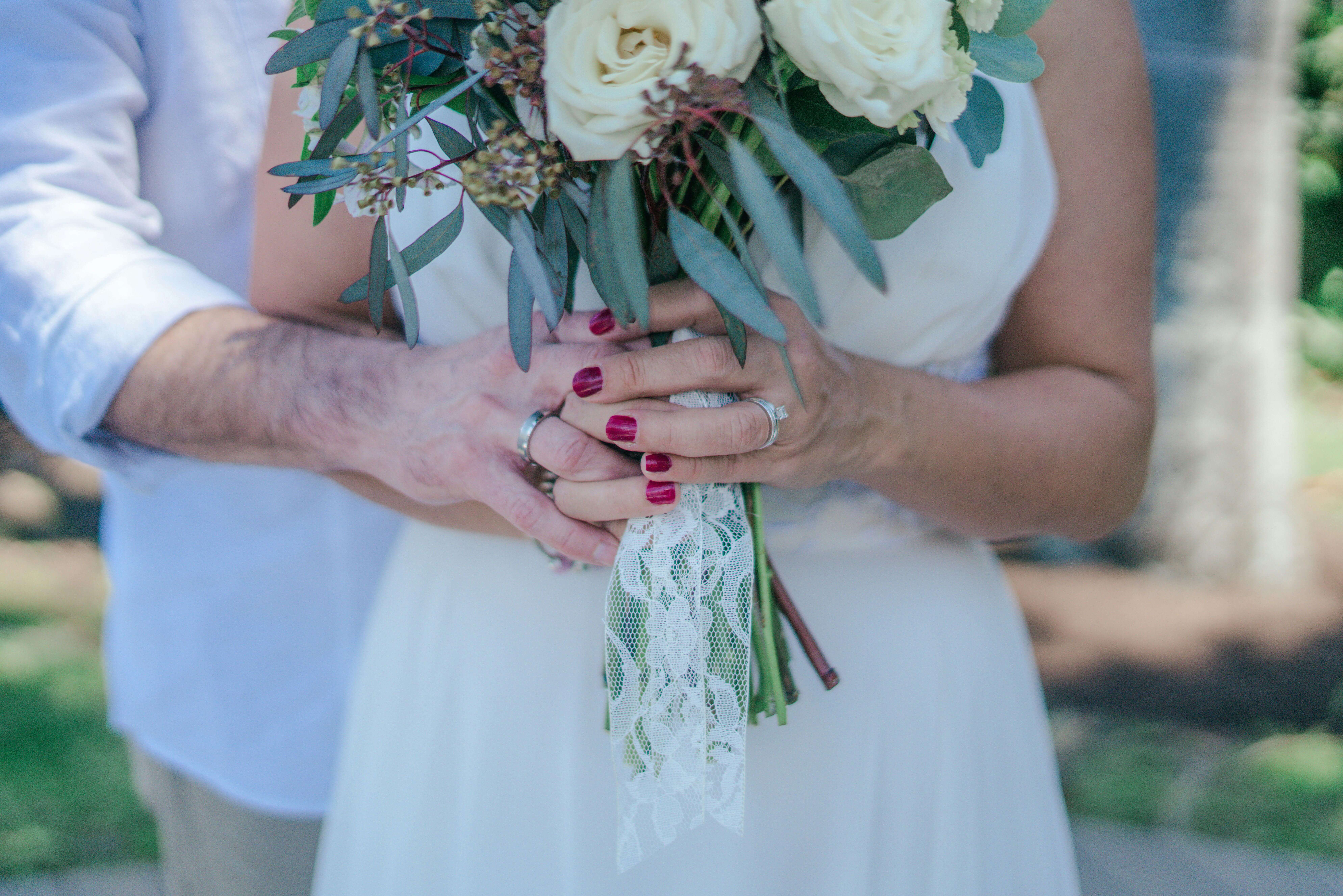 Close-up of a couple holding a bouquet, showcasing wedding rings and elegant attire.