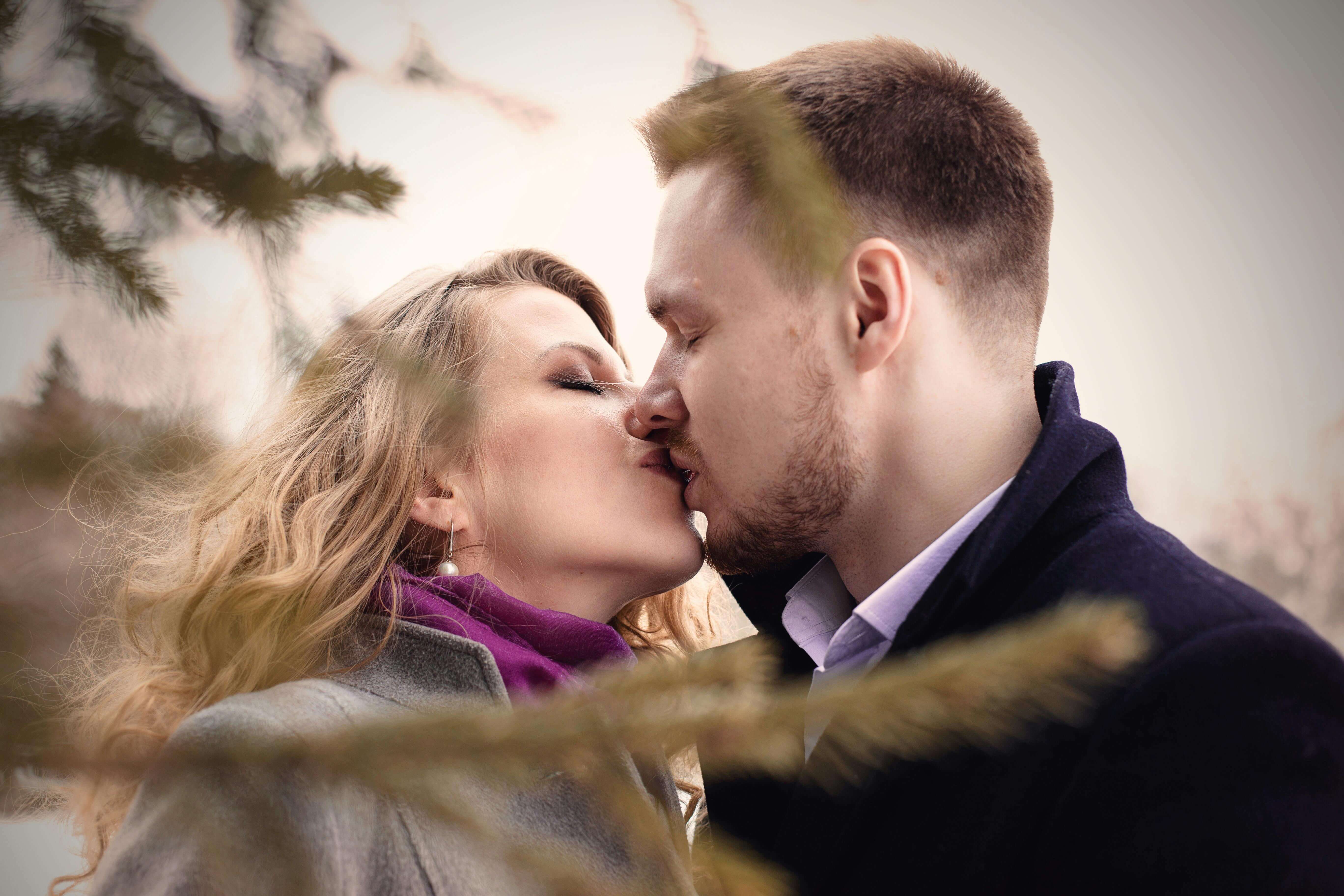 A couple sharing a kiss outdoors, surrounded by winter trees, capturing a moment of love and affection.