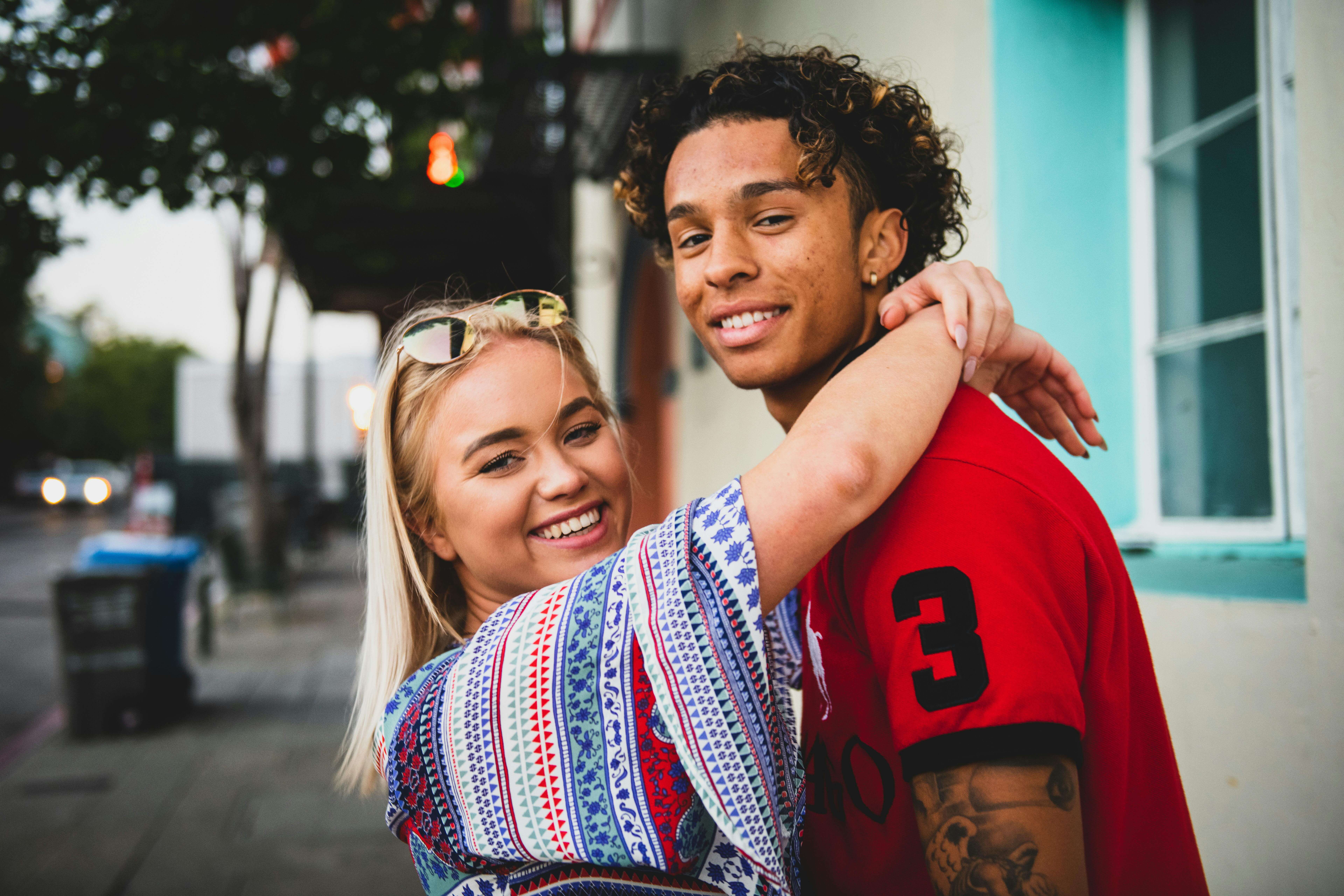 Smiling couple embracing on a colorful street, radiating happiness and affection.