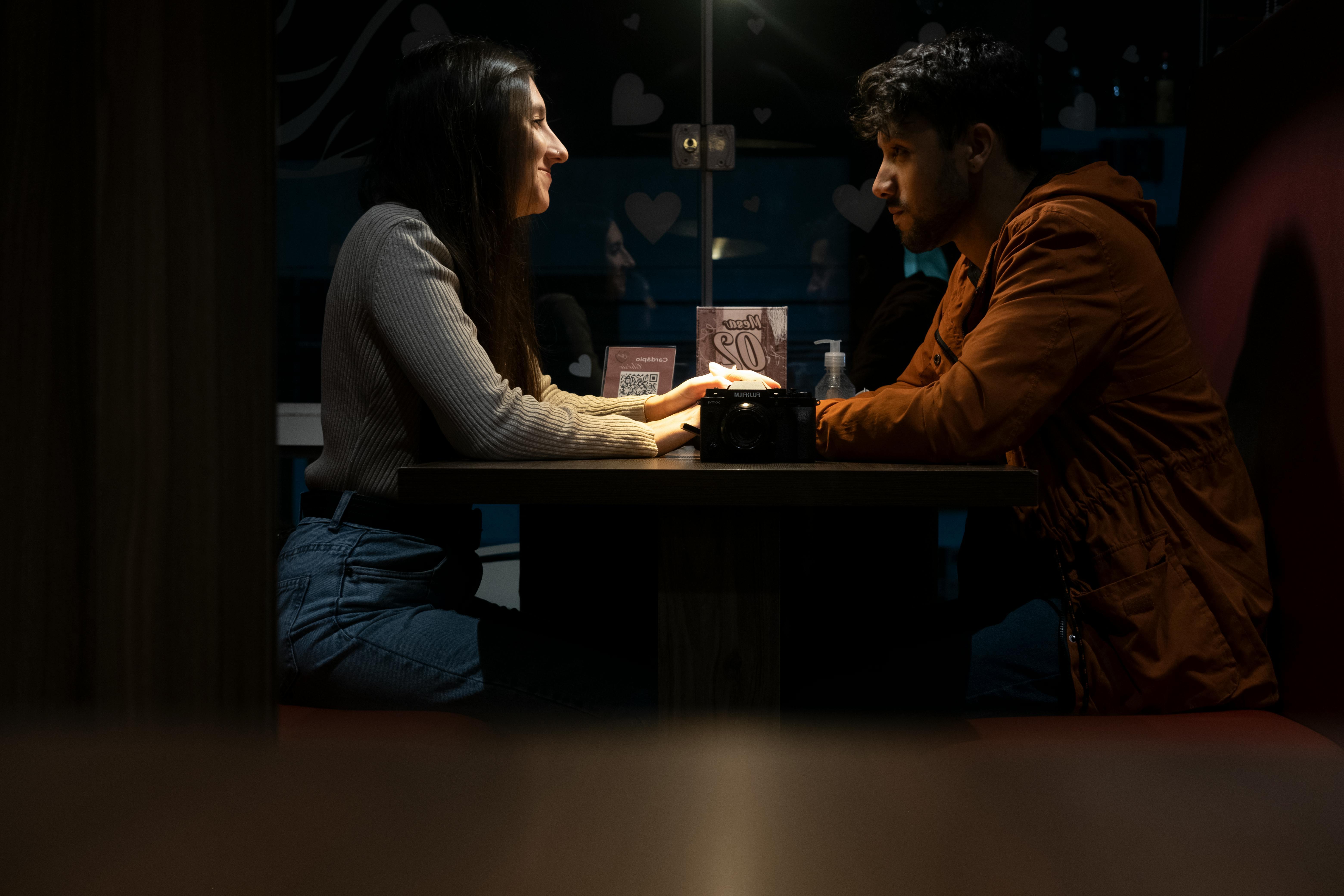 A couple sitting face-to-face, enjoying a romantic evening indoors with intimate lighting.