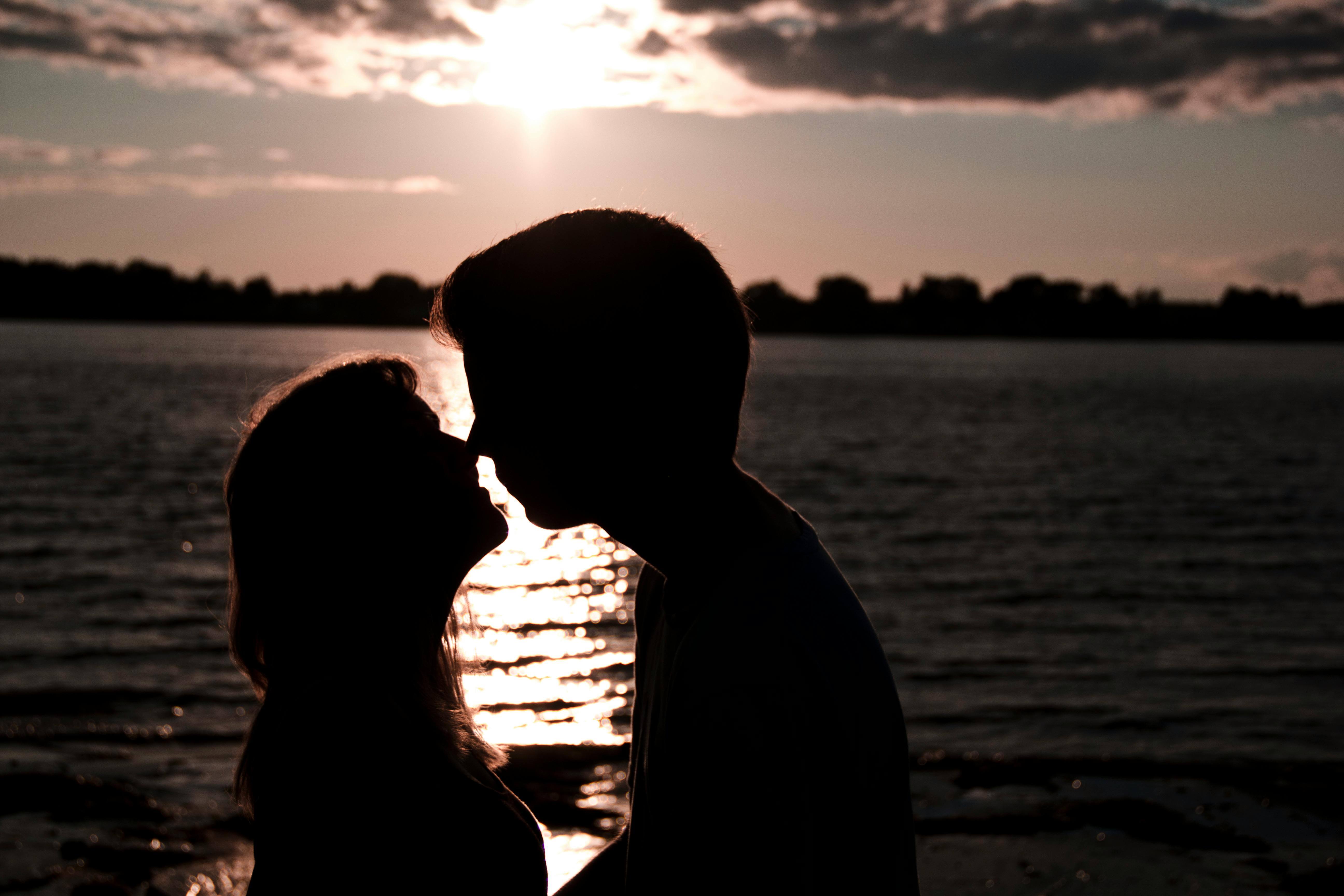 Silhouette of a couple kissing by the lakeside during a breathtaking sunset.