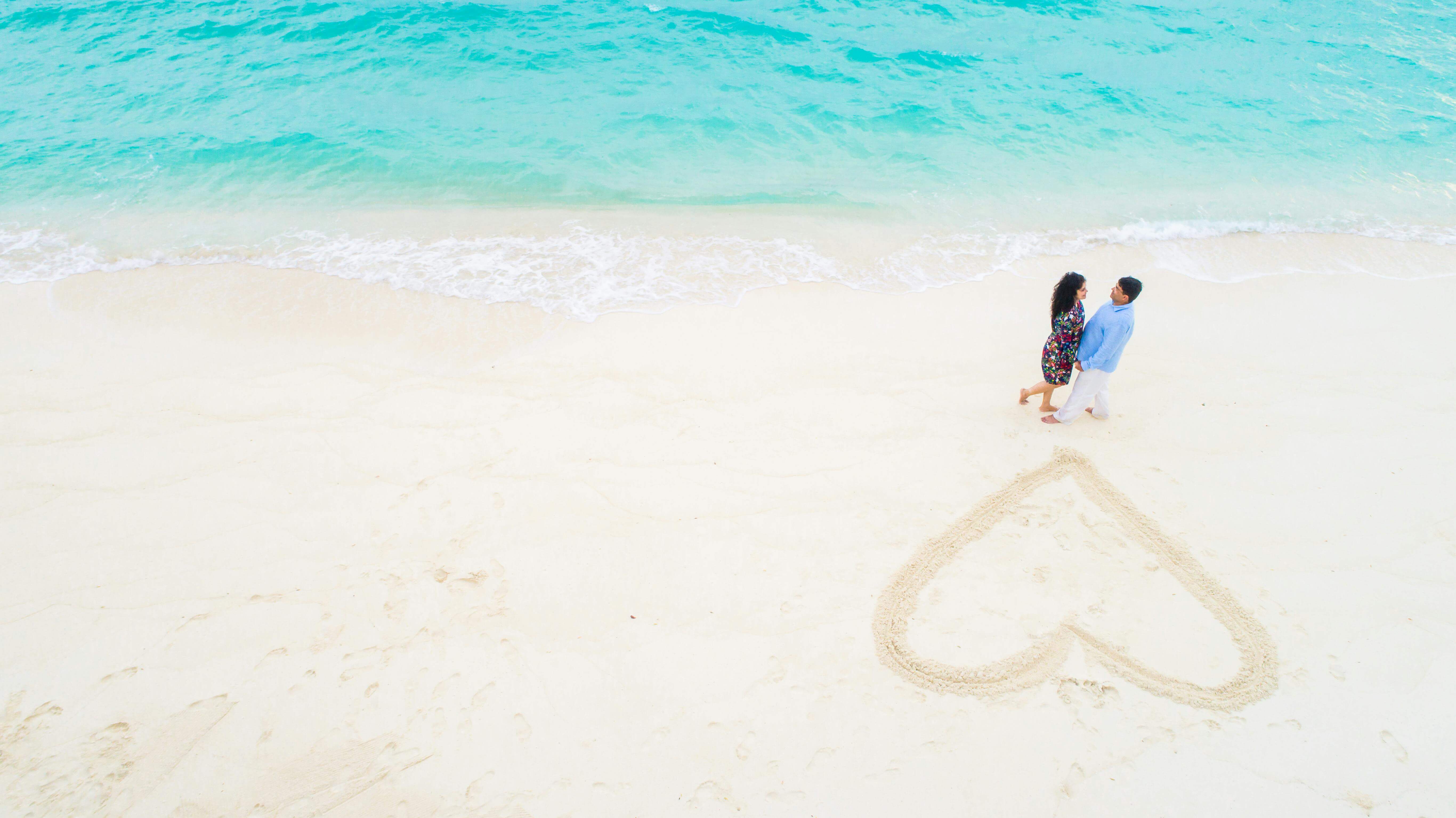 Aerial view of a happy couple on a picturesque Maldives beach with a heart drawn in the sand.