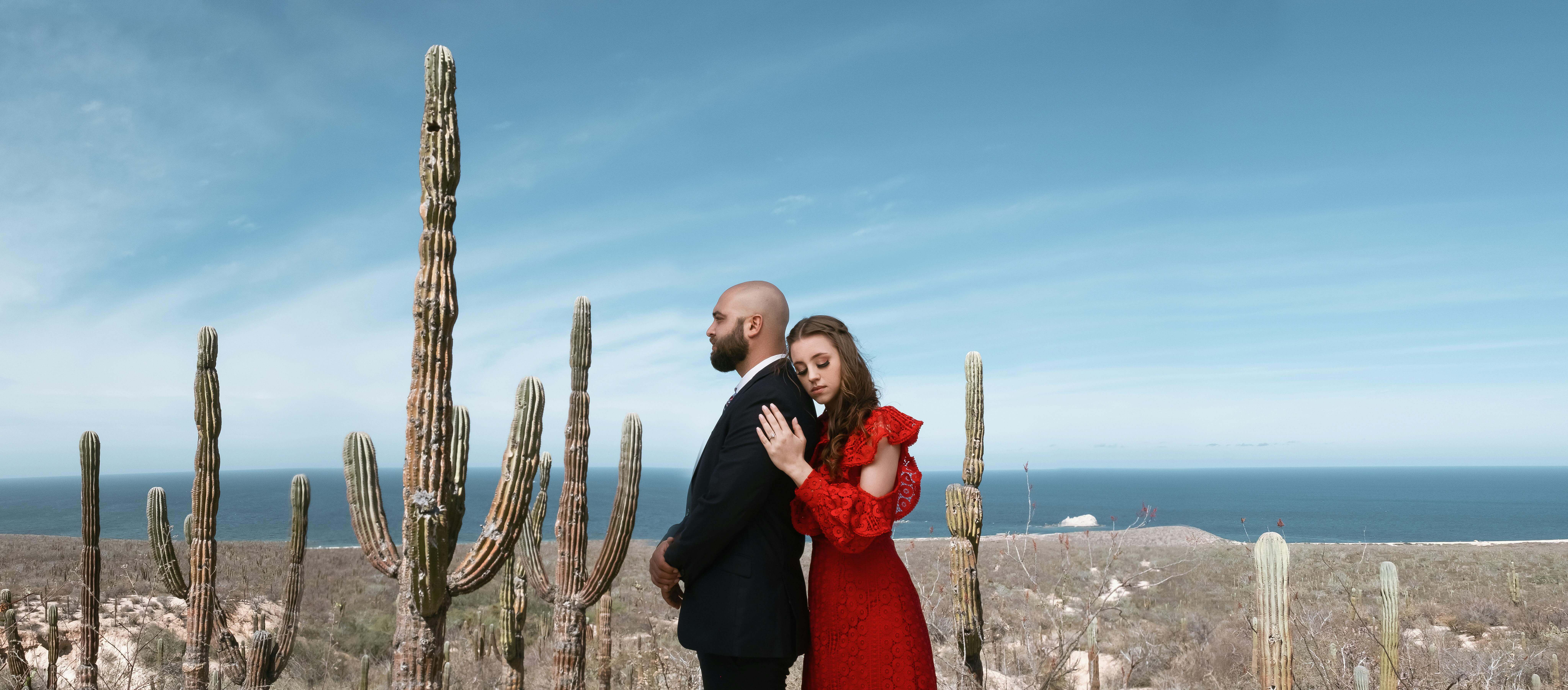 A couple embraces amid La Paz's desert landscape with cacti and ocean in view.