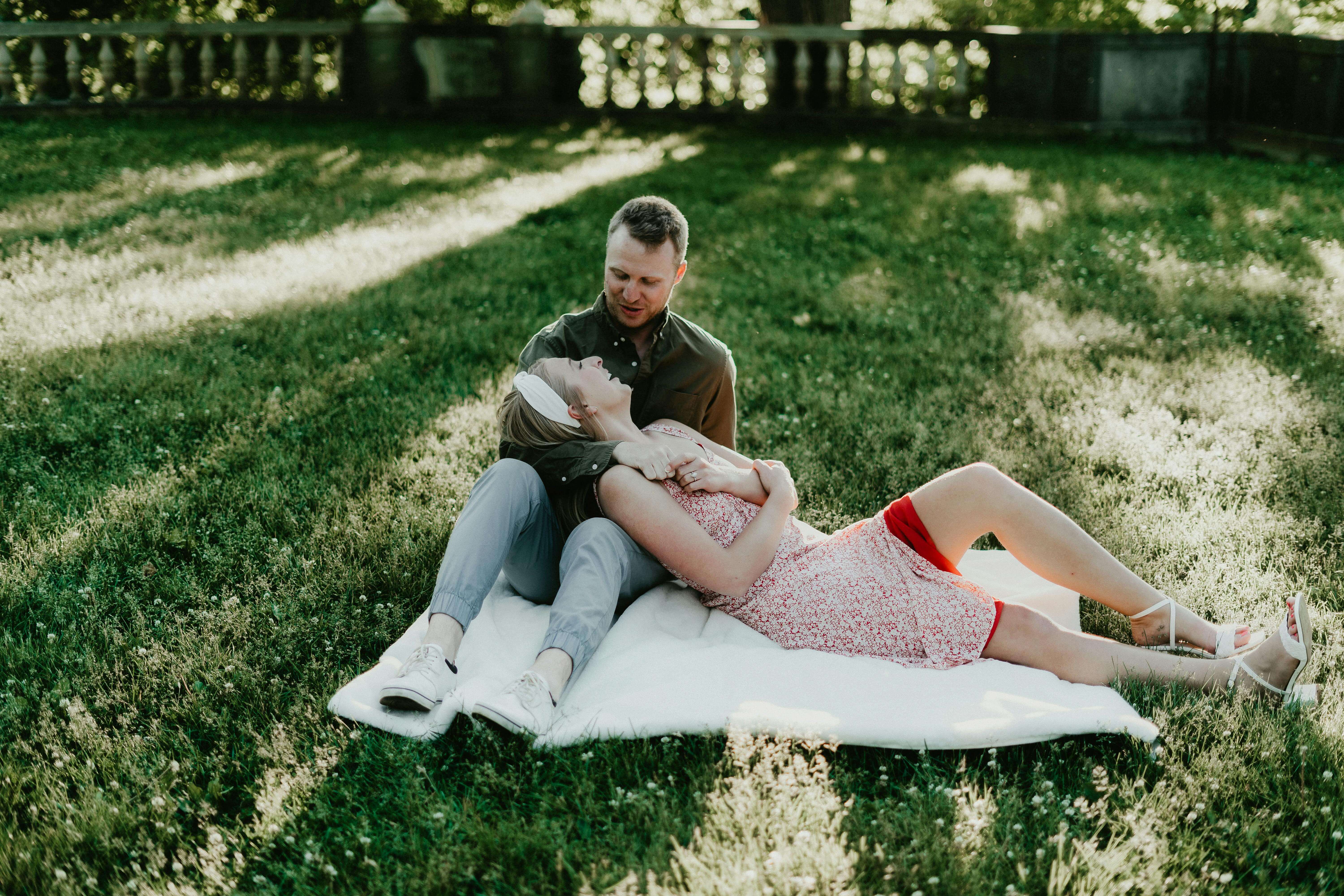 A loving couple enjoys a sunny day lying on a blanket in a grassy park.