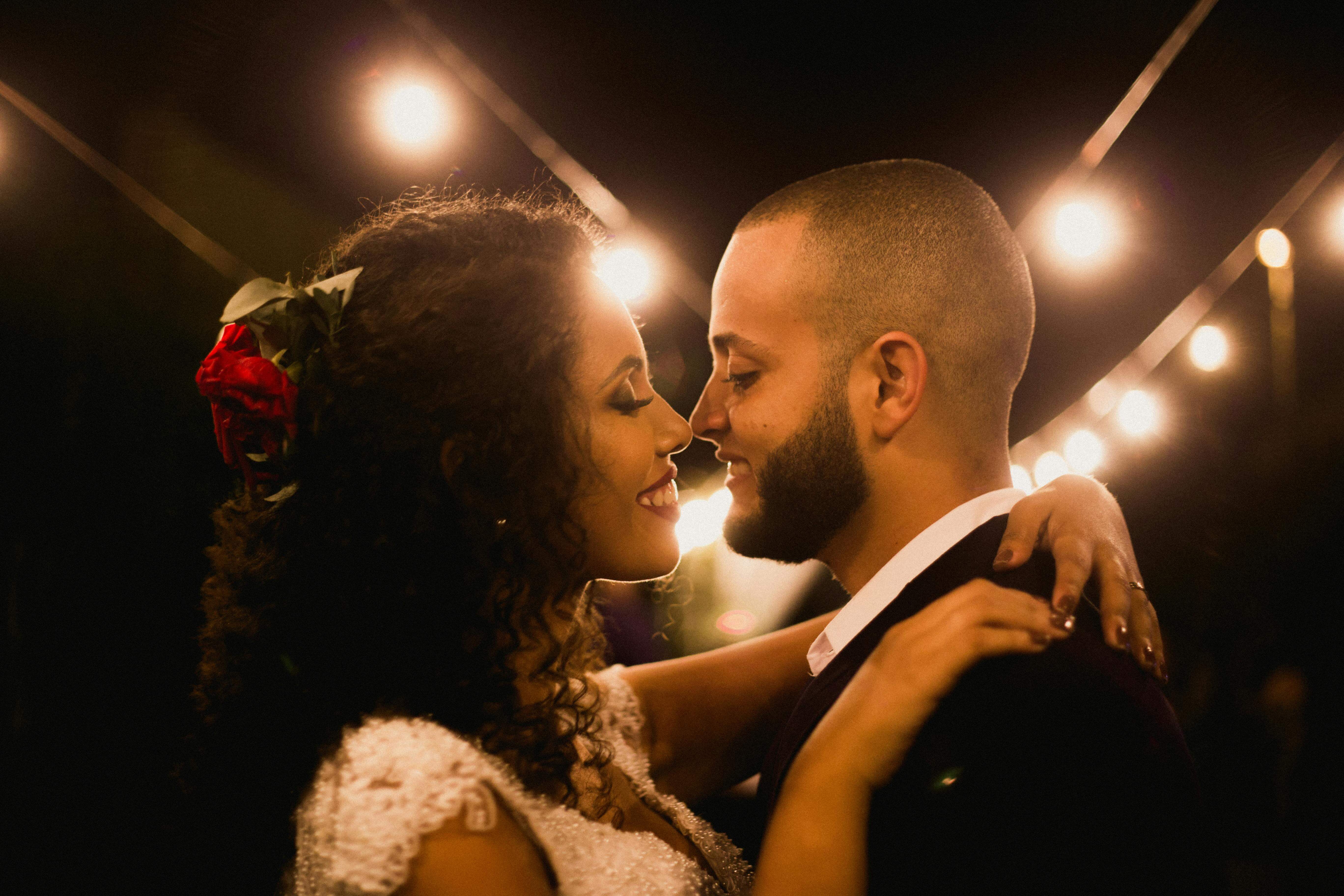 A joyful wedding couple embracing under romantic string lights at night.