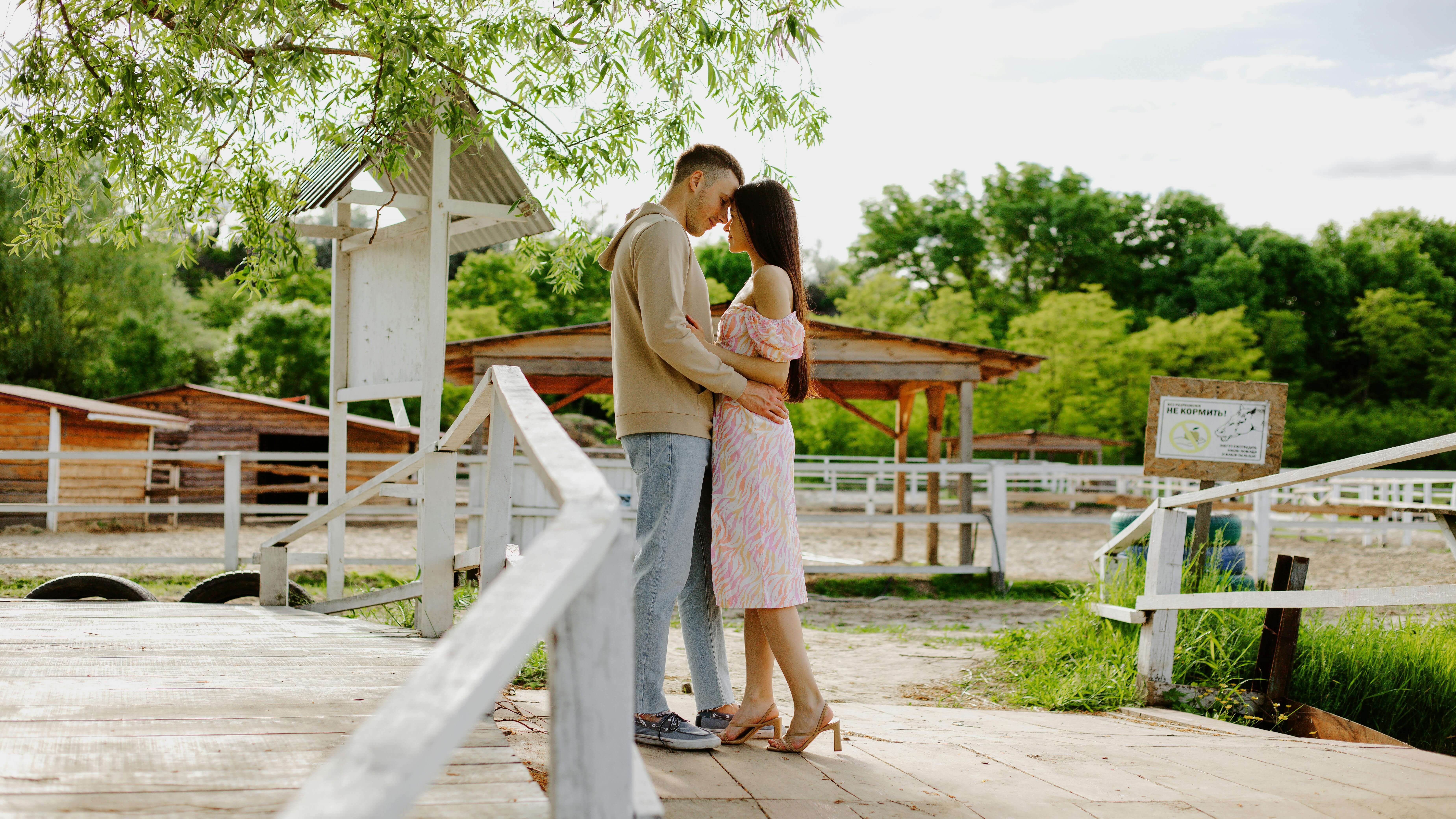 Young couple embraces outdoors on a sunny day by a rustic wooden fence, symbolizing love.