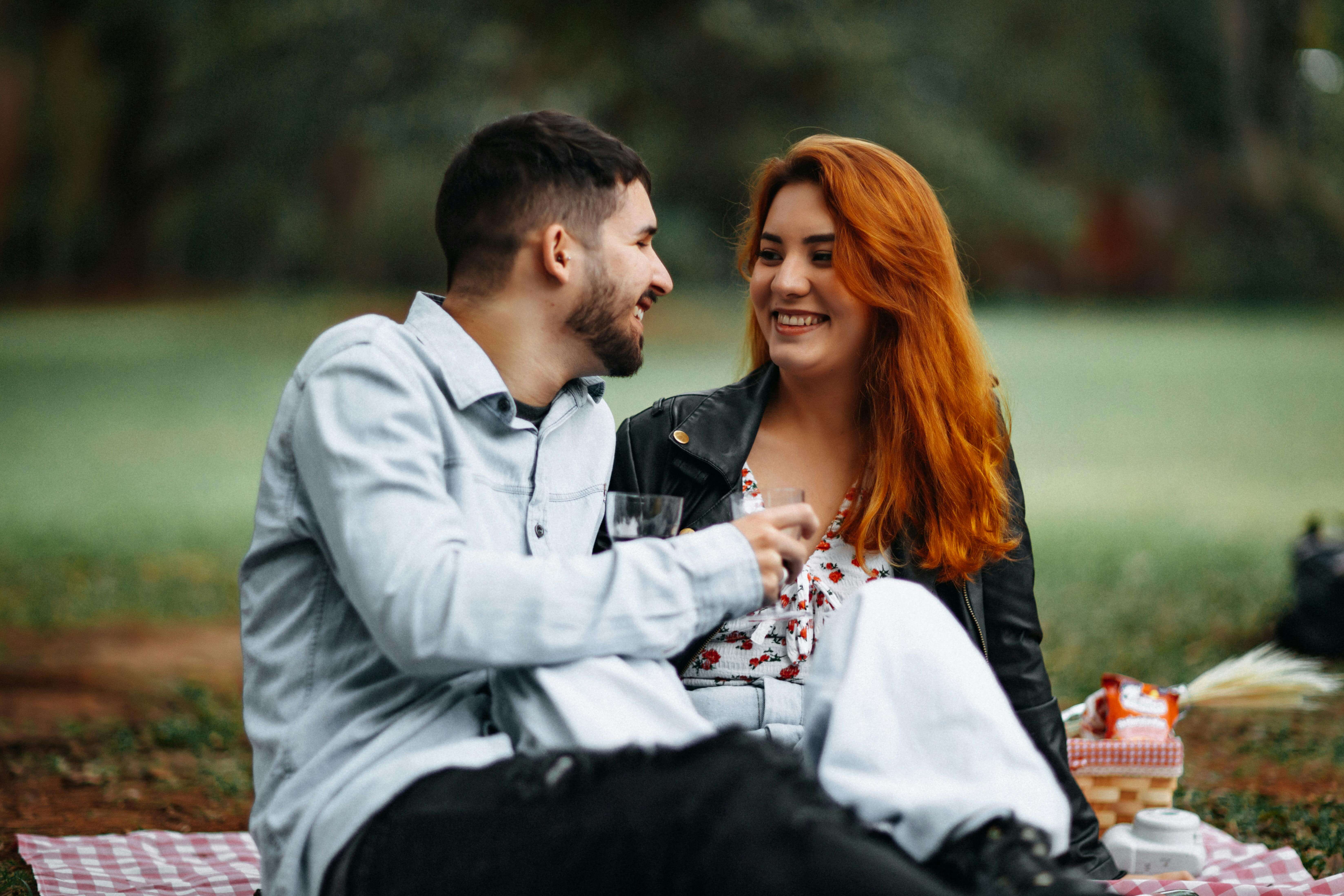 Happy couple enjoying a romantic picnic outdoors with wine and smiles.