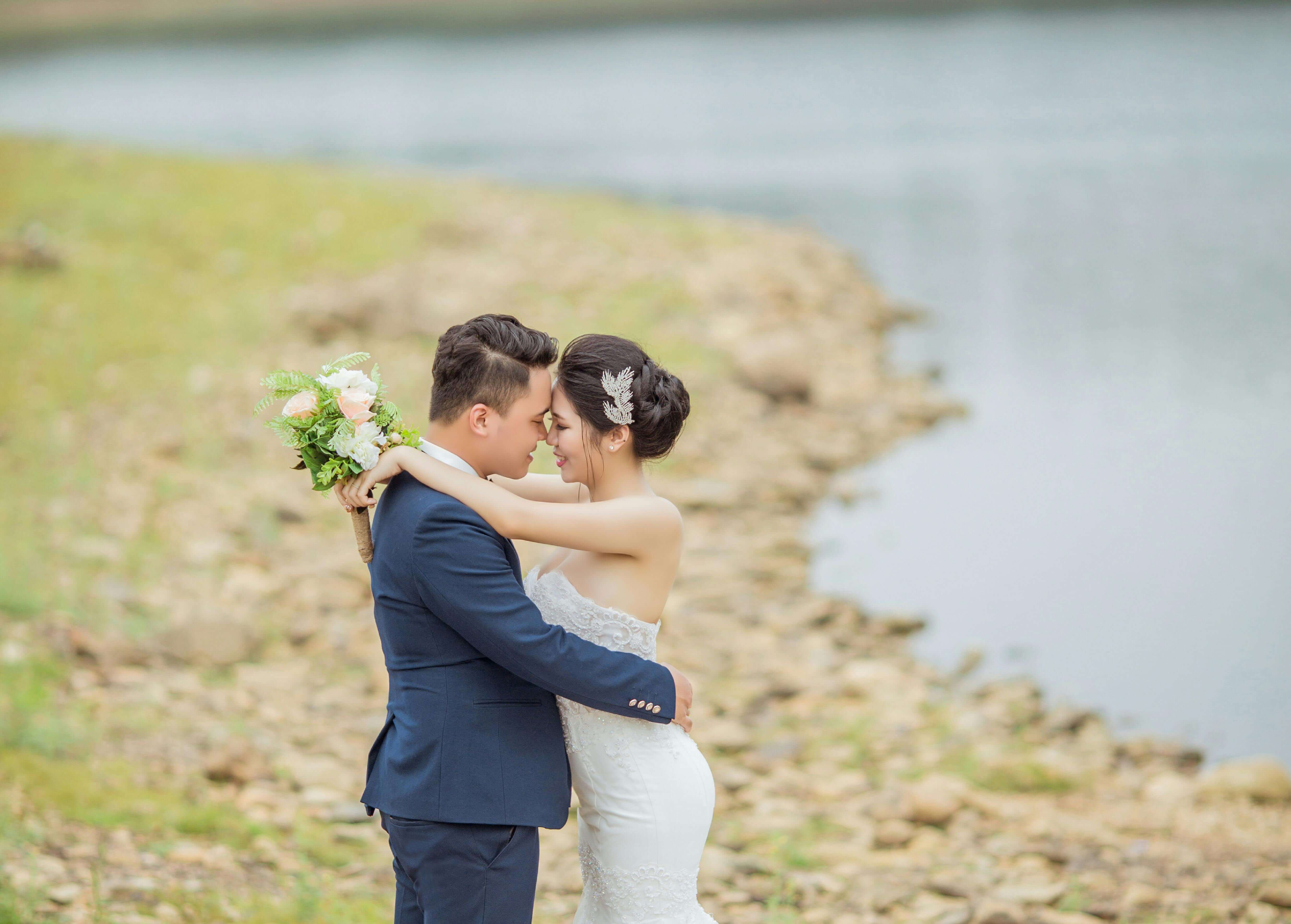 A bride and groom embrace romantically by a lakeside. Perfect wedding capture.