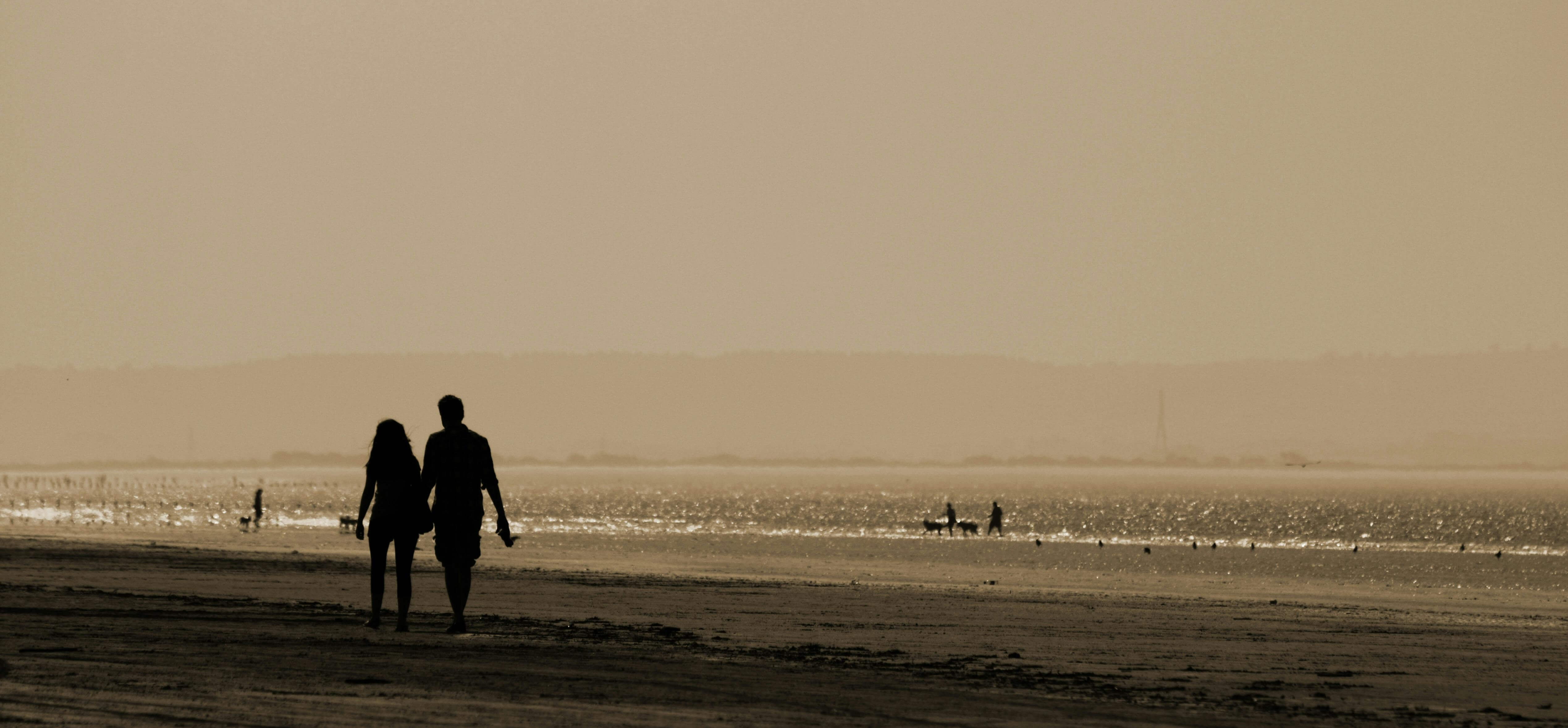 Silhouette of a couple walking hand in hand along a serene beach at sunset, capturing a romantic and tranquil moment.