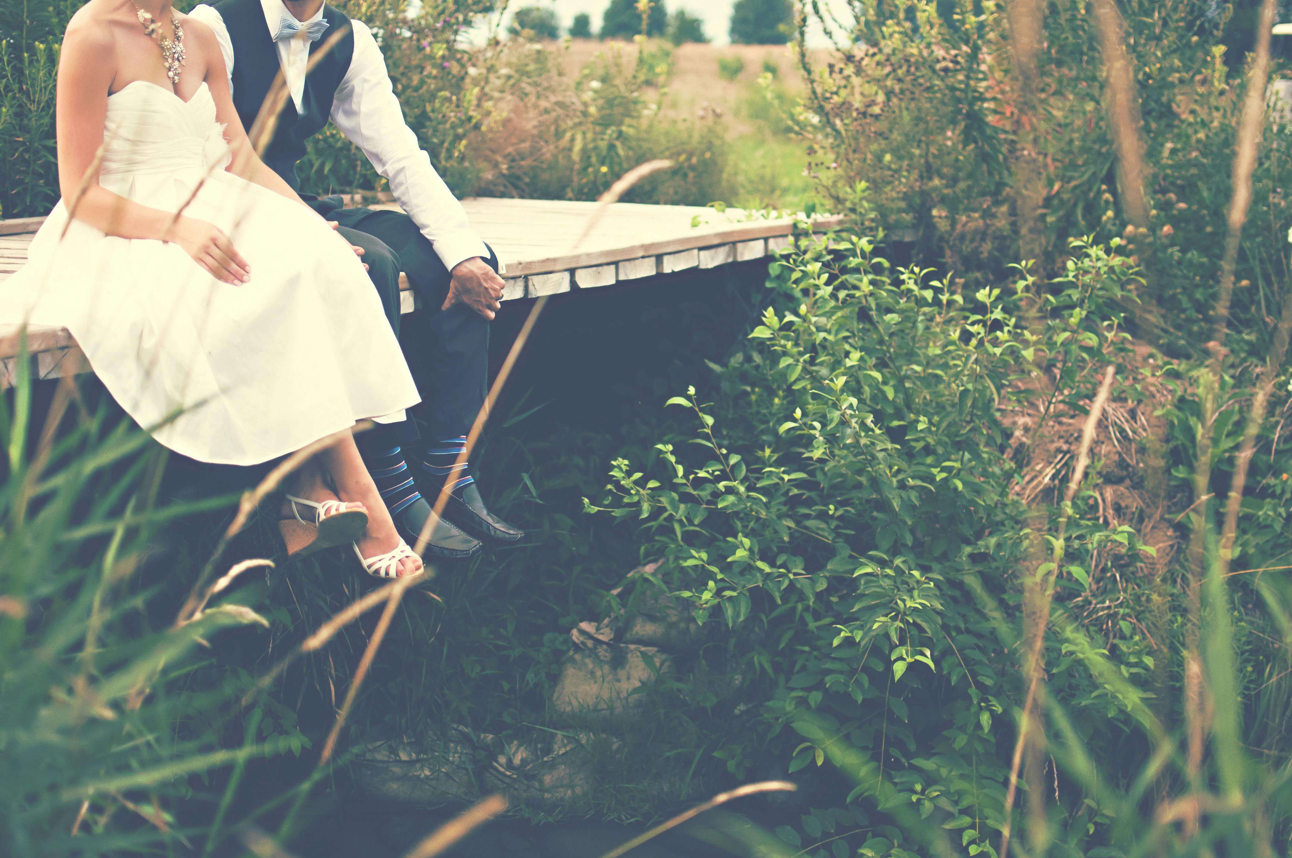 Bride and groom sitting by the water in a serene outdoor setting, symbolizing love and nature.