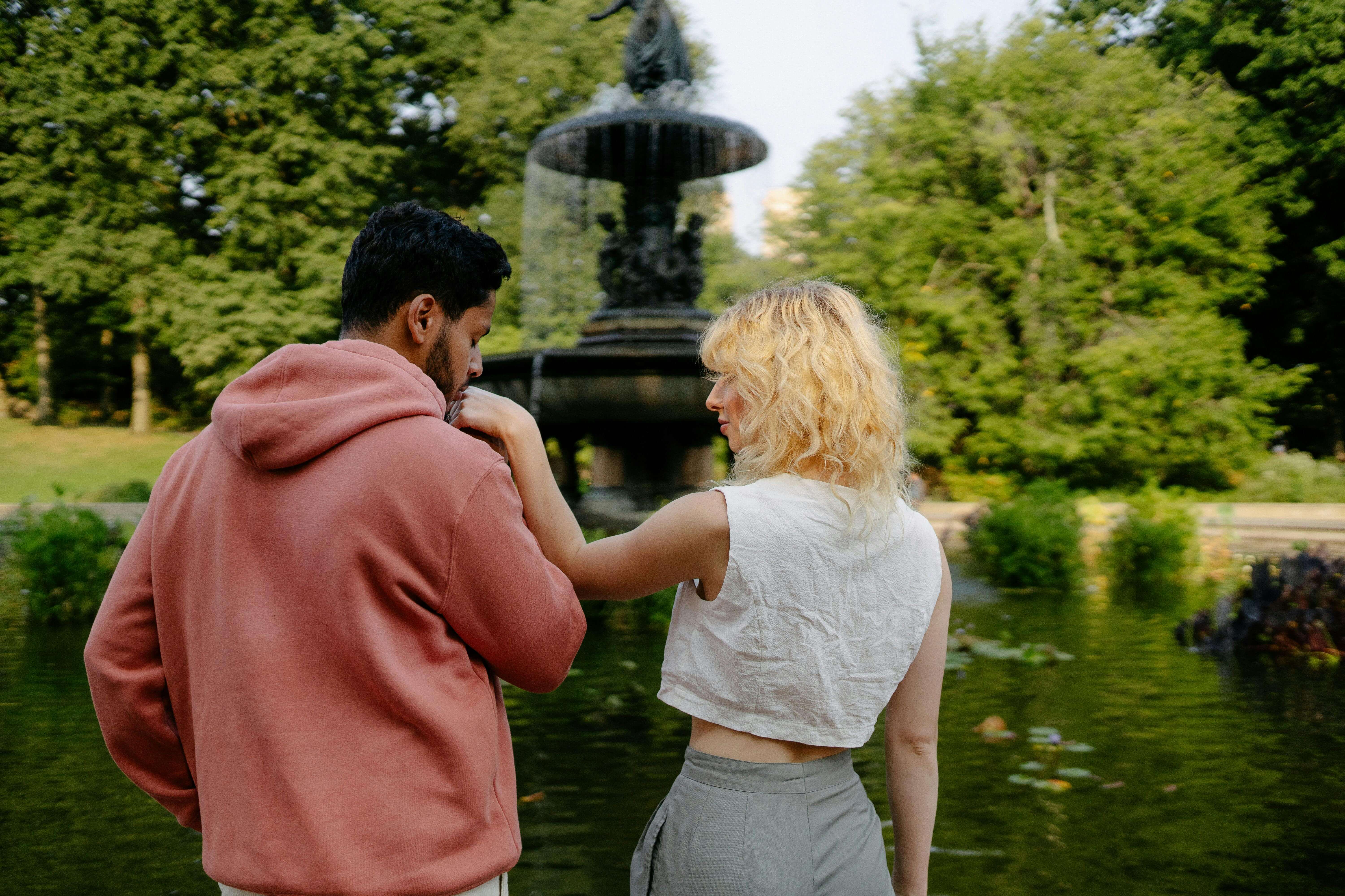 A couple shares a tender moment by a fountain in a lush park setting.
