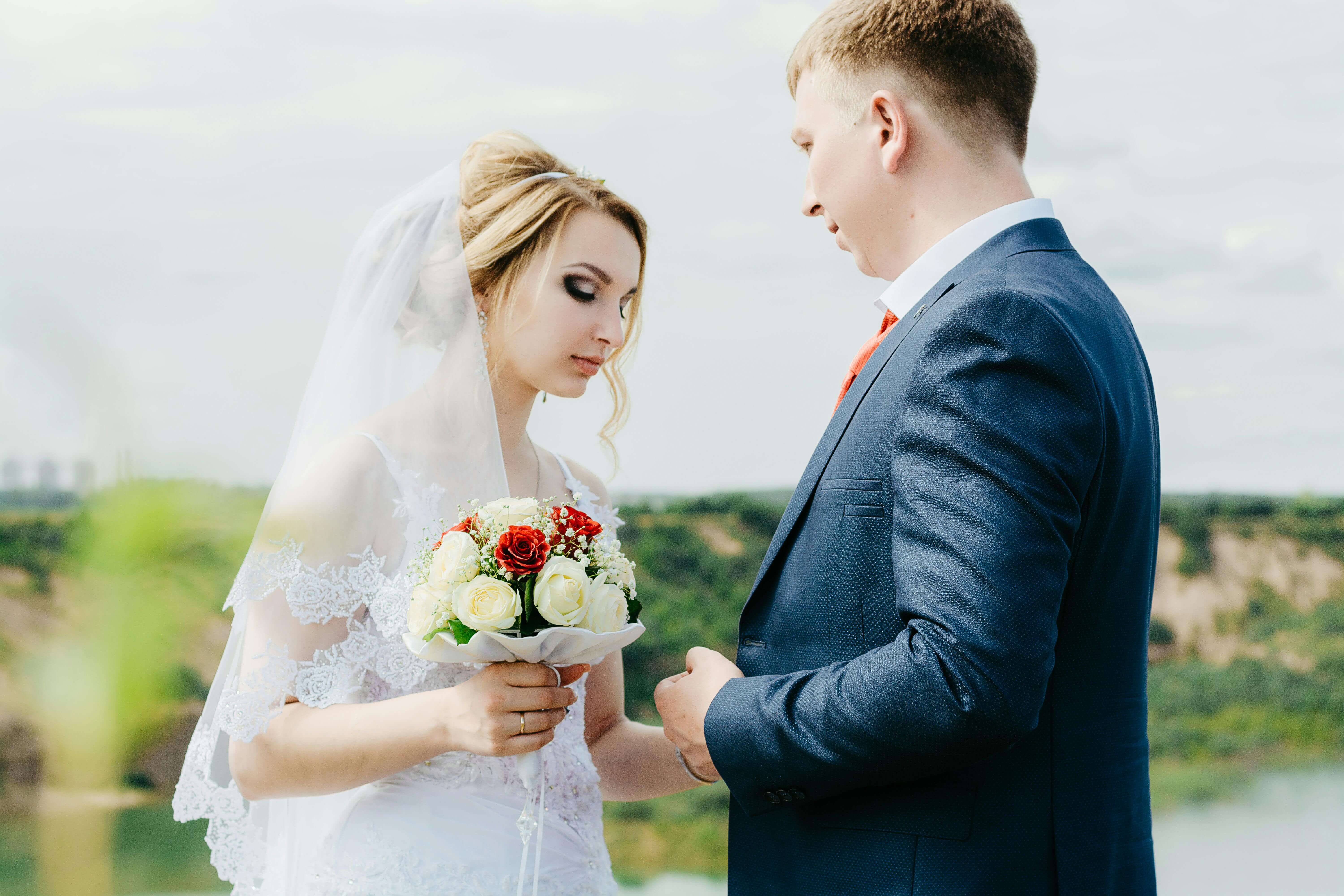 Beautiful outdoor portrait of bride and groom in wedding attire holding bouquet.
