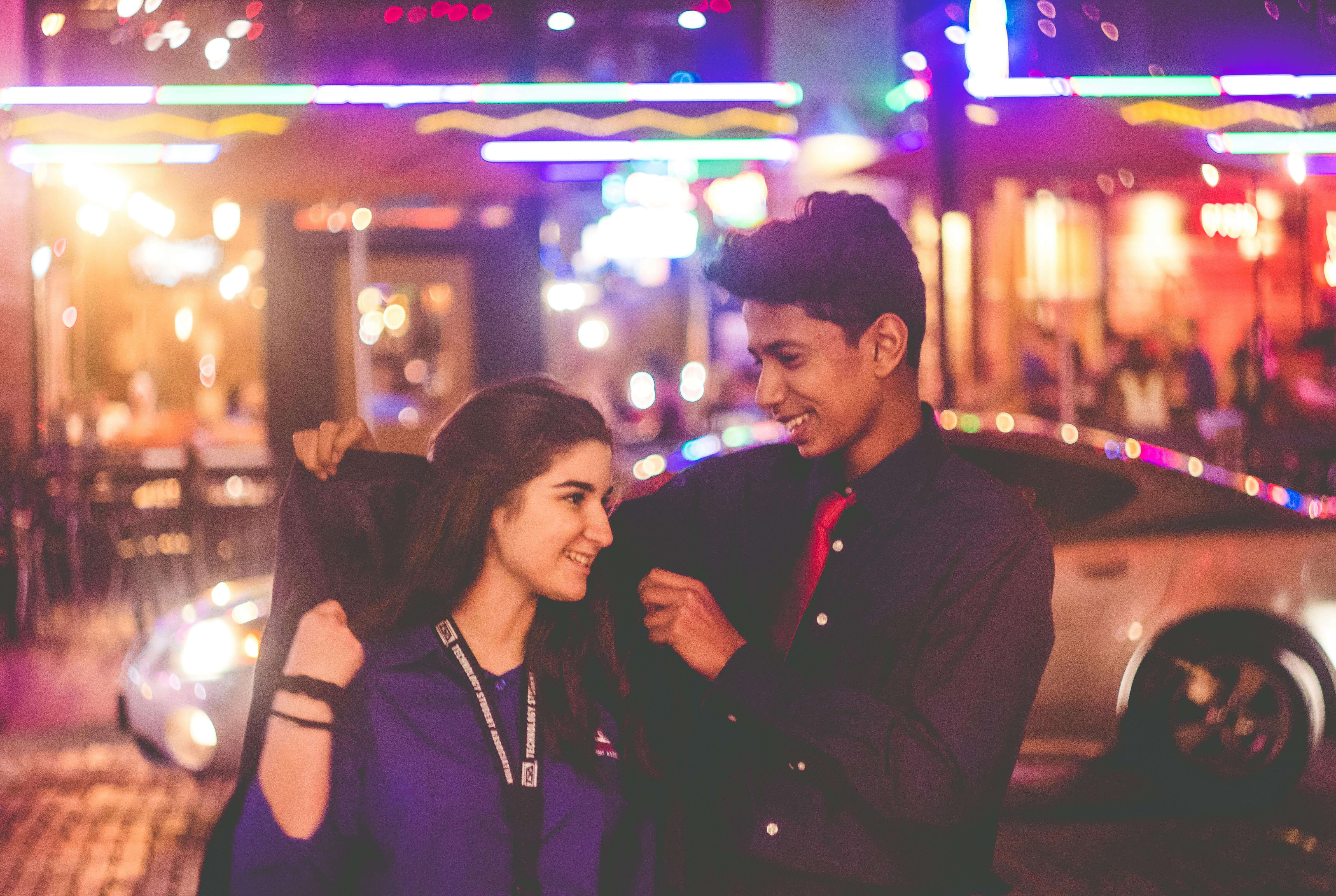 A young couple smiles warmly under vibrant city lights in Fort Worth, Texas.