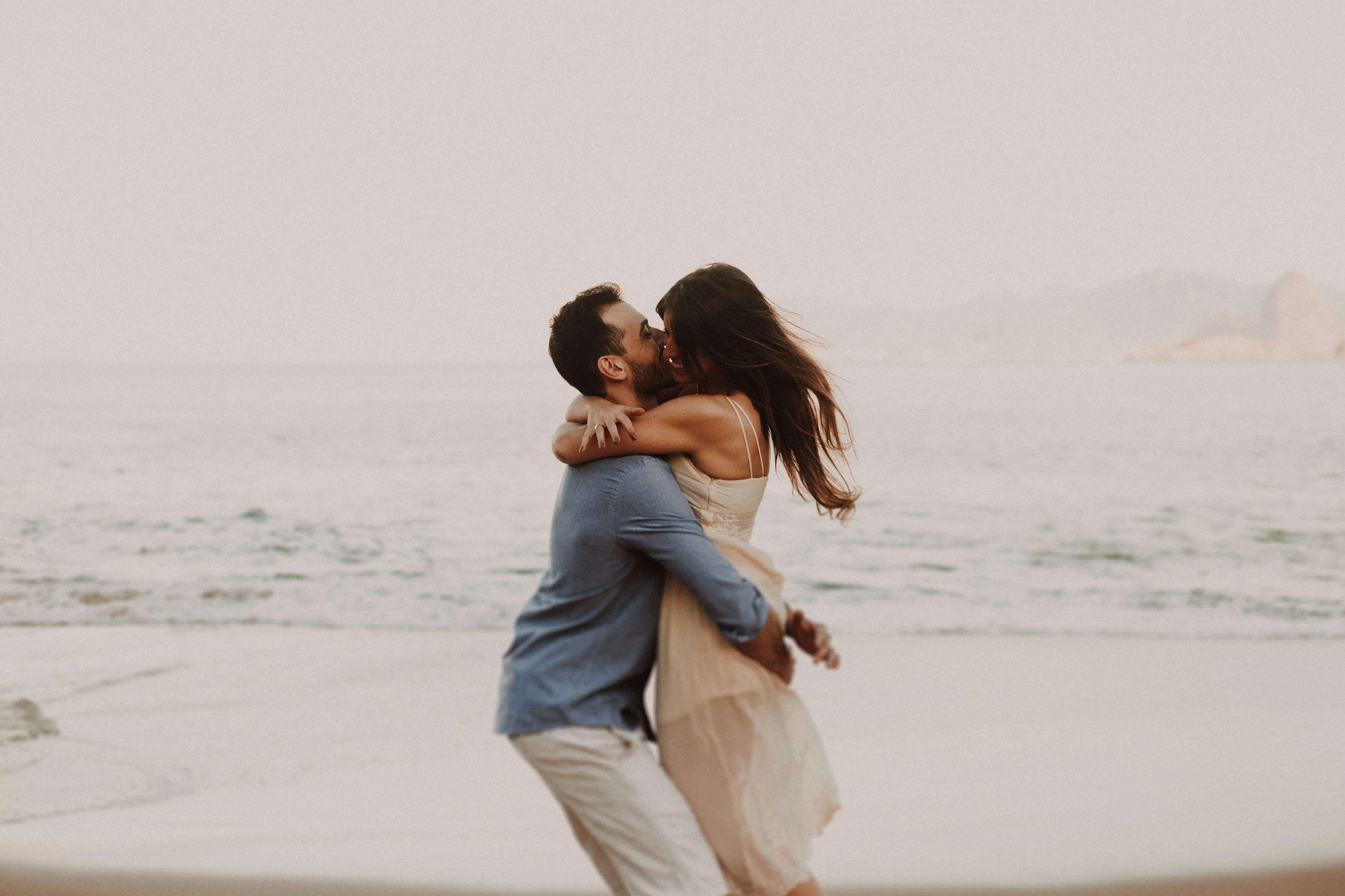 A couple shares a romantic embrace by the ocean, capturing a moment of love.