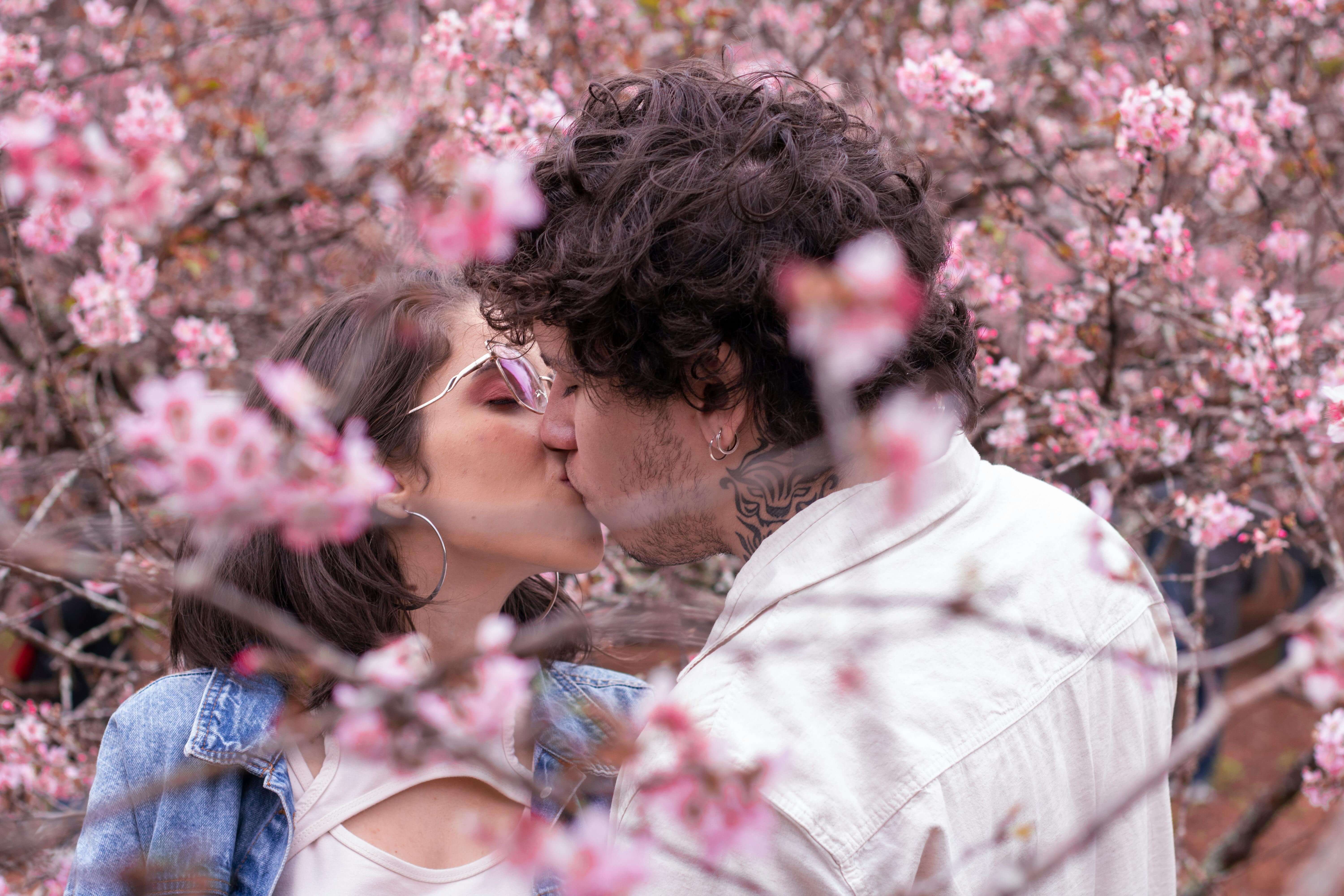 A young couple sharing a kiss surrounded by blooming cherry blossoms in spring.