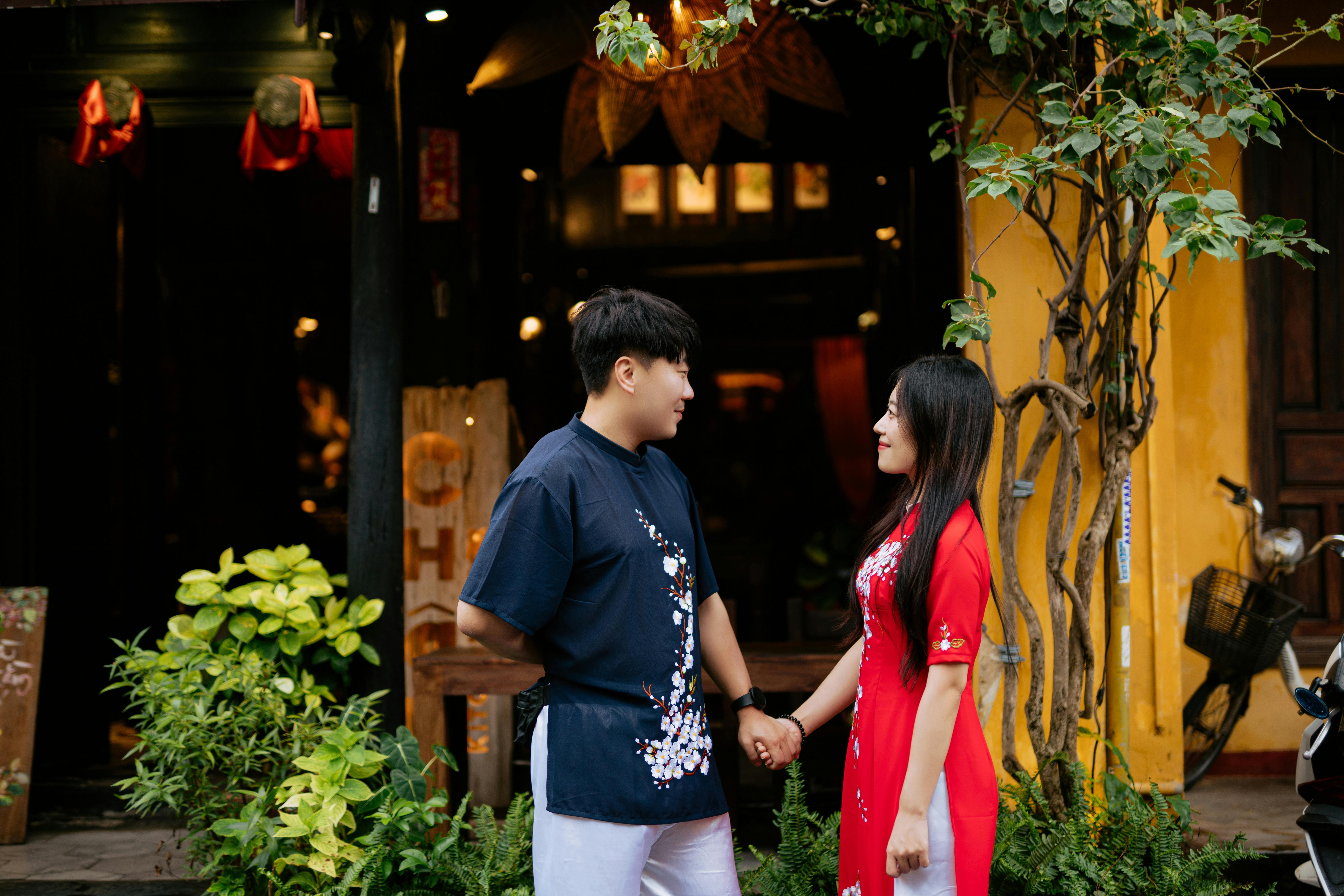 A couple holding hands outdoors in traditional Vietnamese clothing surrounded by greenery.