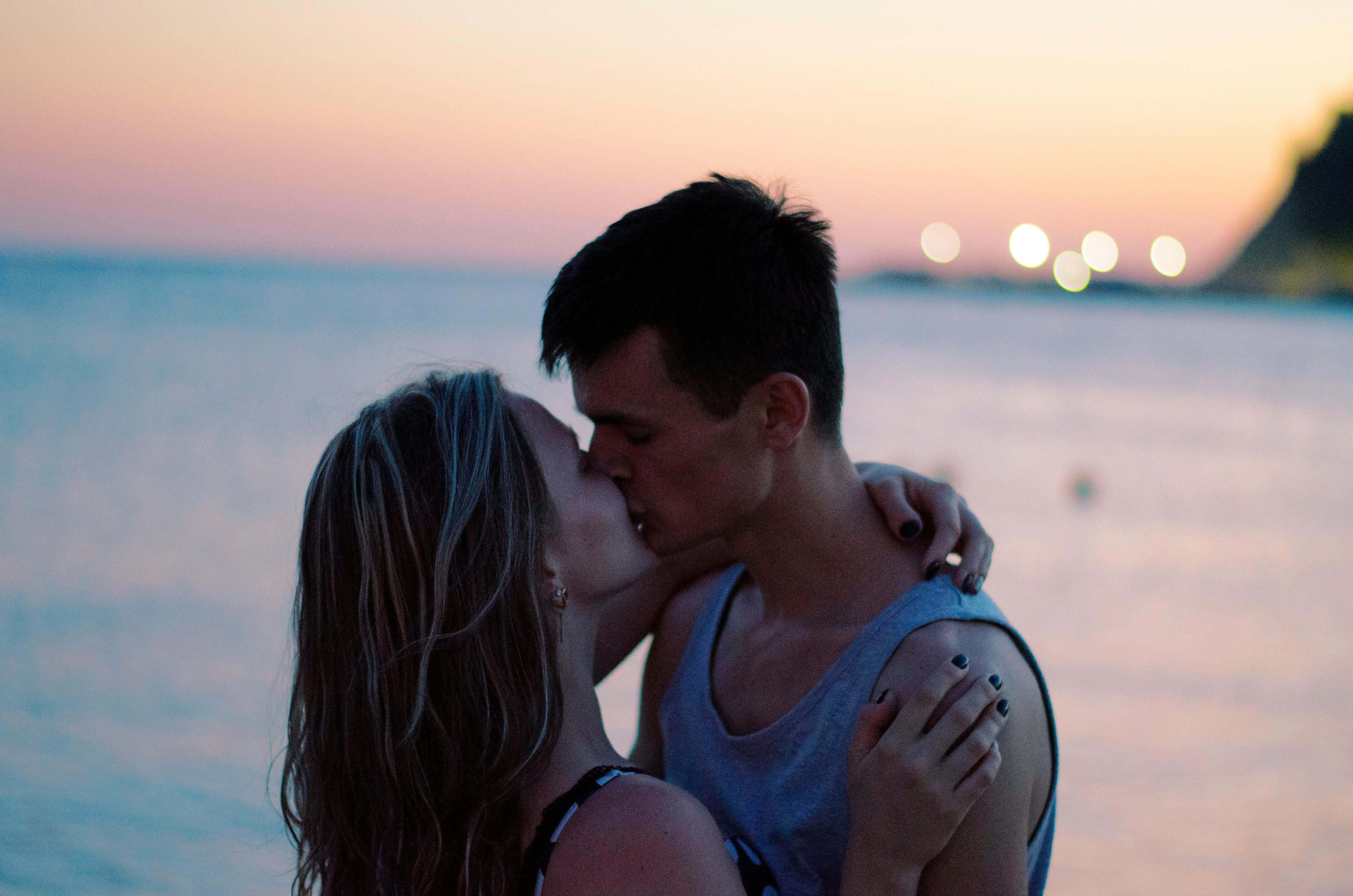 A couple shares a romantic kiss at the beach during sunset, capturing love and intimacy.
