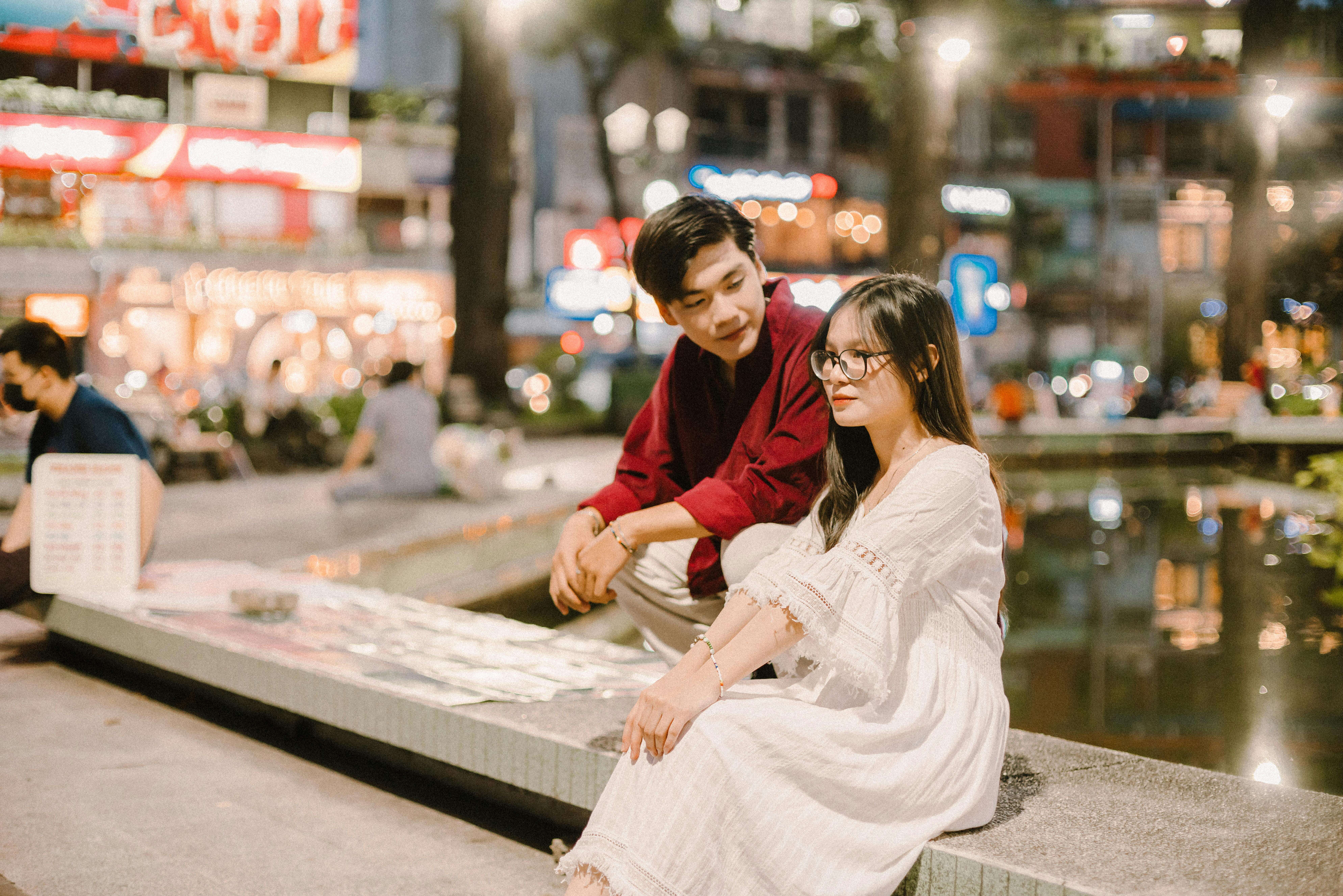 A young couple enjoying an evening in a lively city square with neon lights.