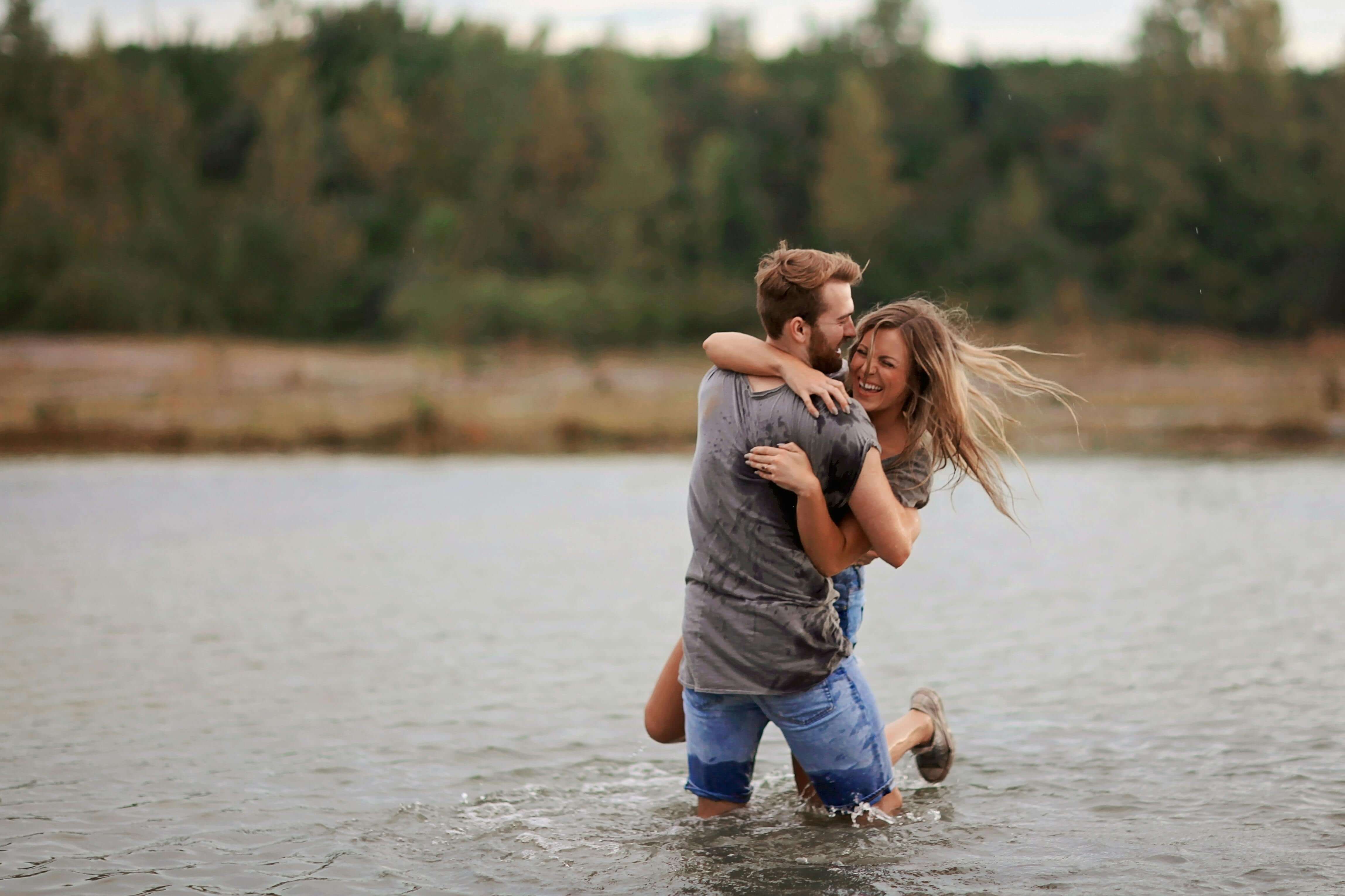 A young couple joyfully playing in the water against a natural backdrop, embodying love and happiness.