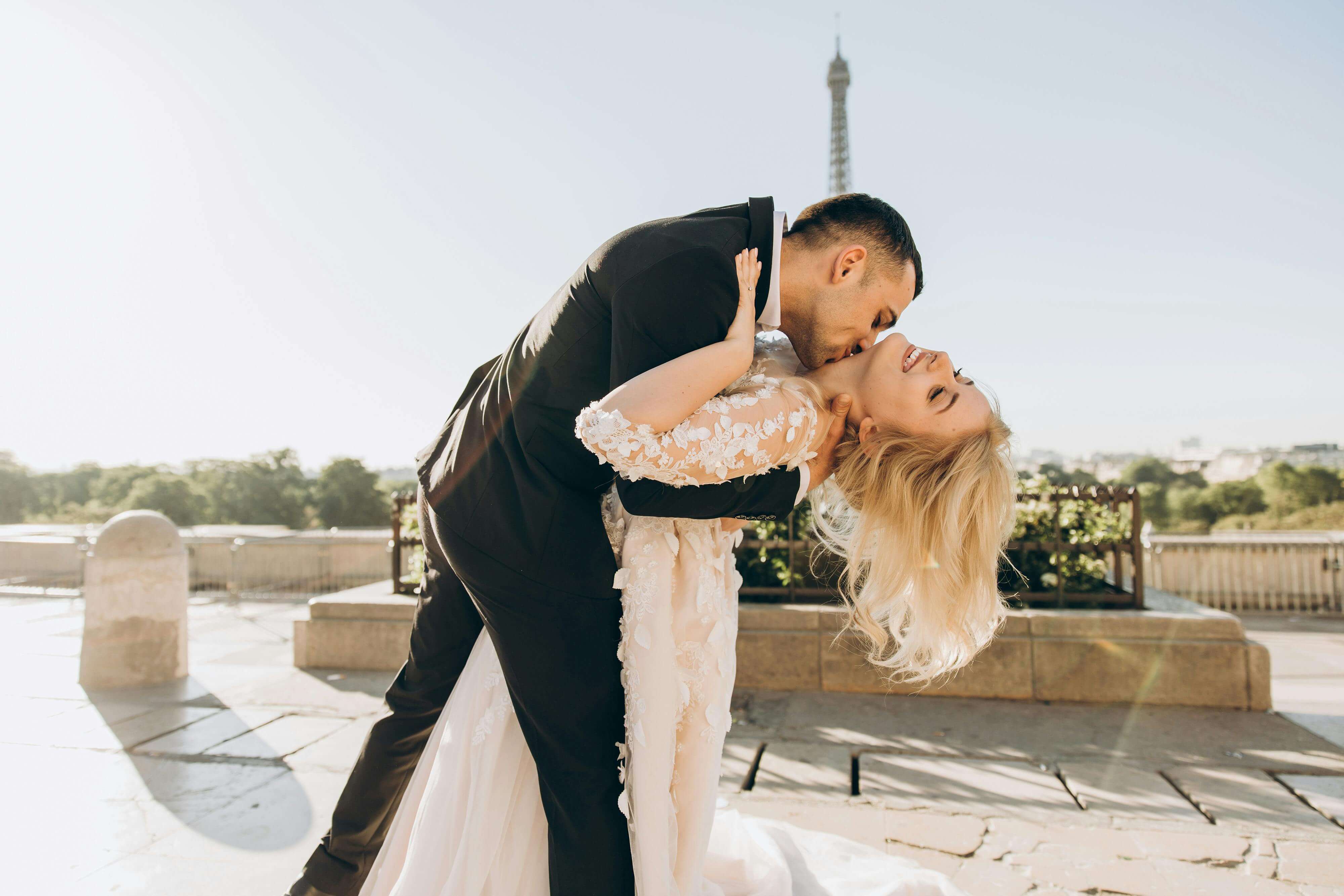 A joyful bride and groom kiss with the Eiffel Tower in the background, symbolizing love and togetherness in Paris.