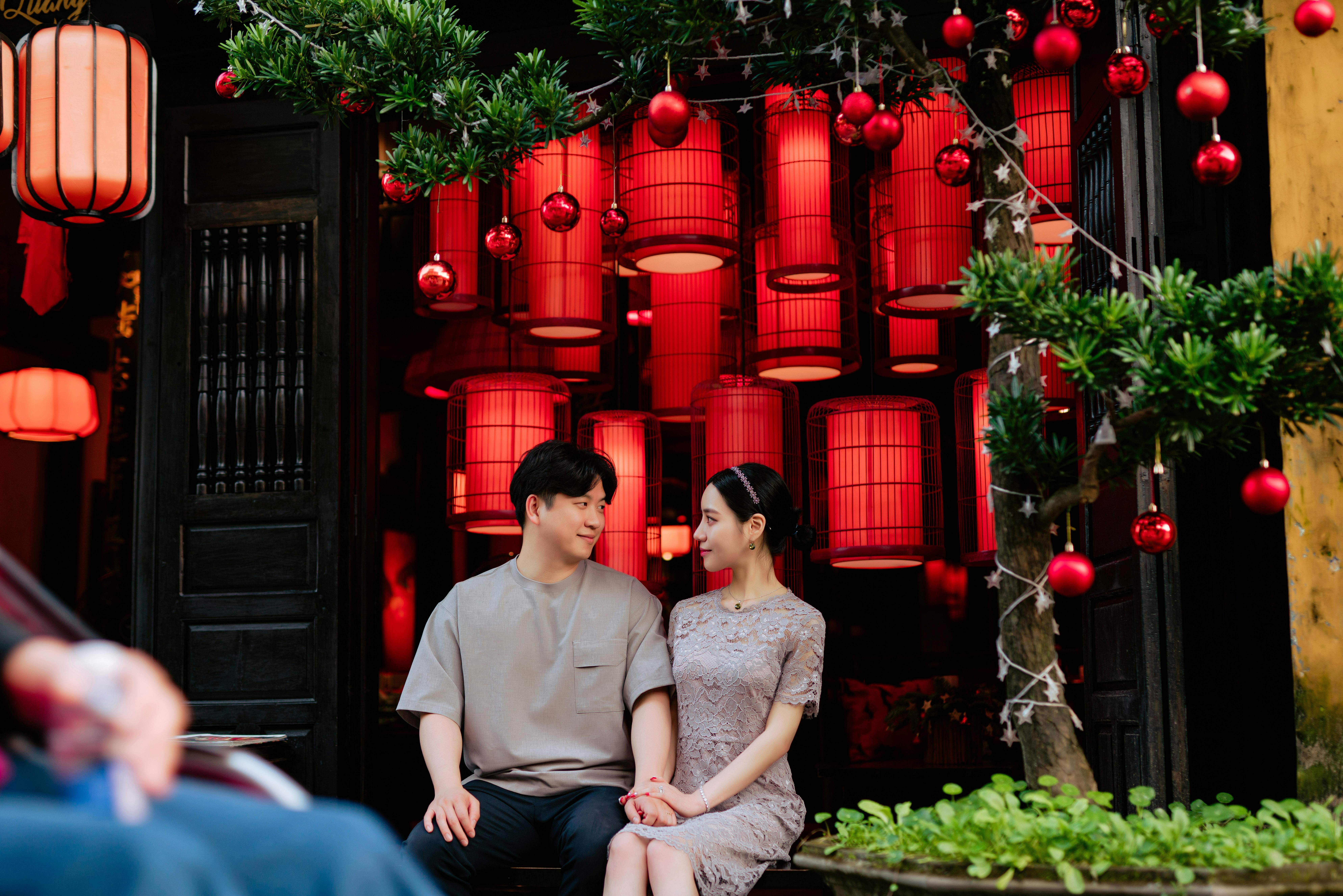 A couple enjoys a romantic moment surrounded by red Chinese lanterns in a vibrant setting.