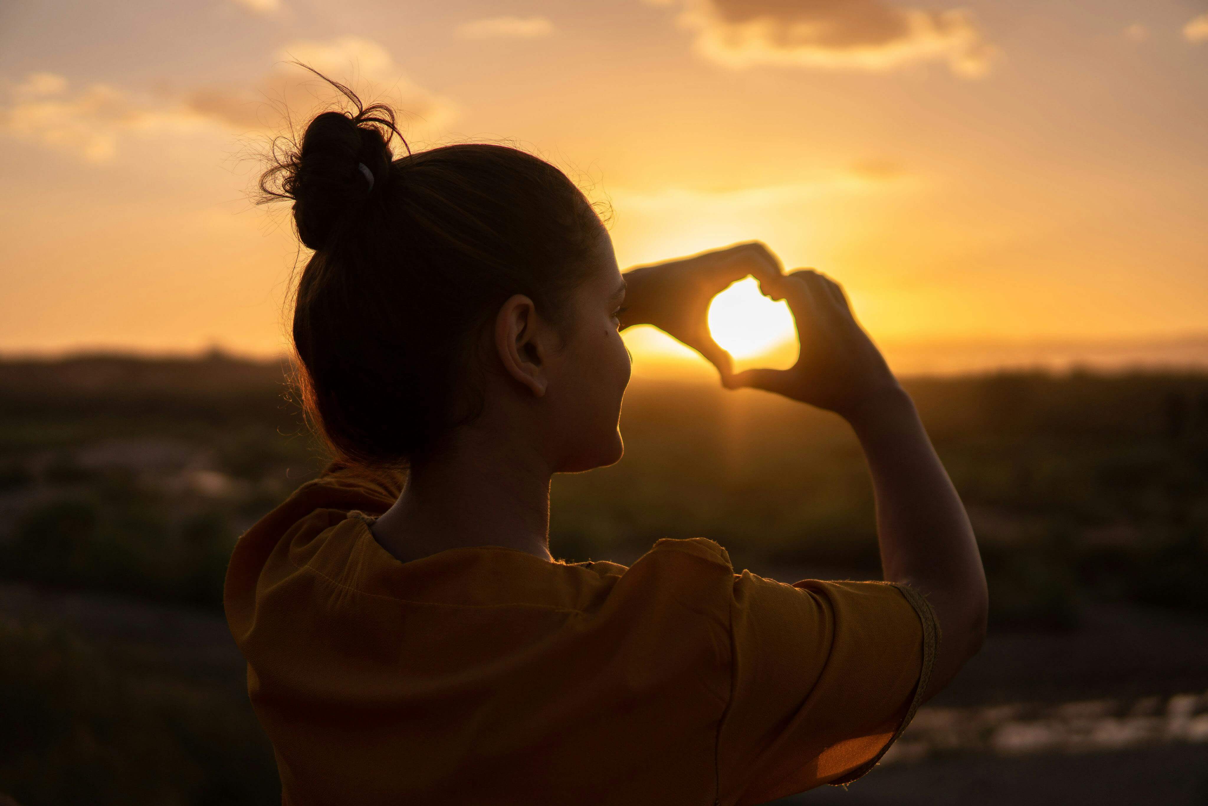 A silhouette of a young woman forming a heart shape at sunset in KelÃ¢at M'Gouna, Morocco.