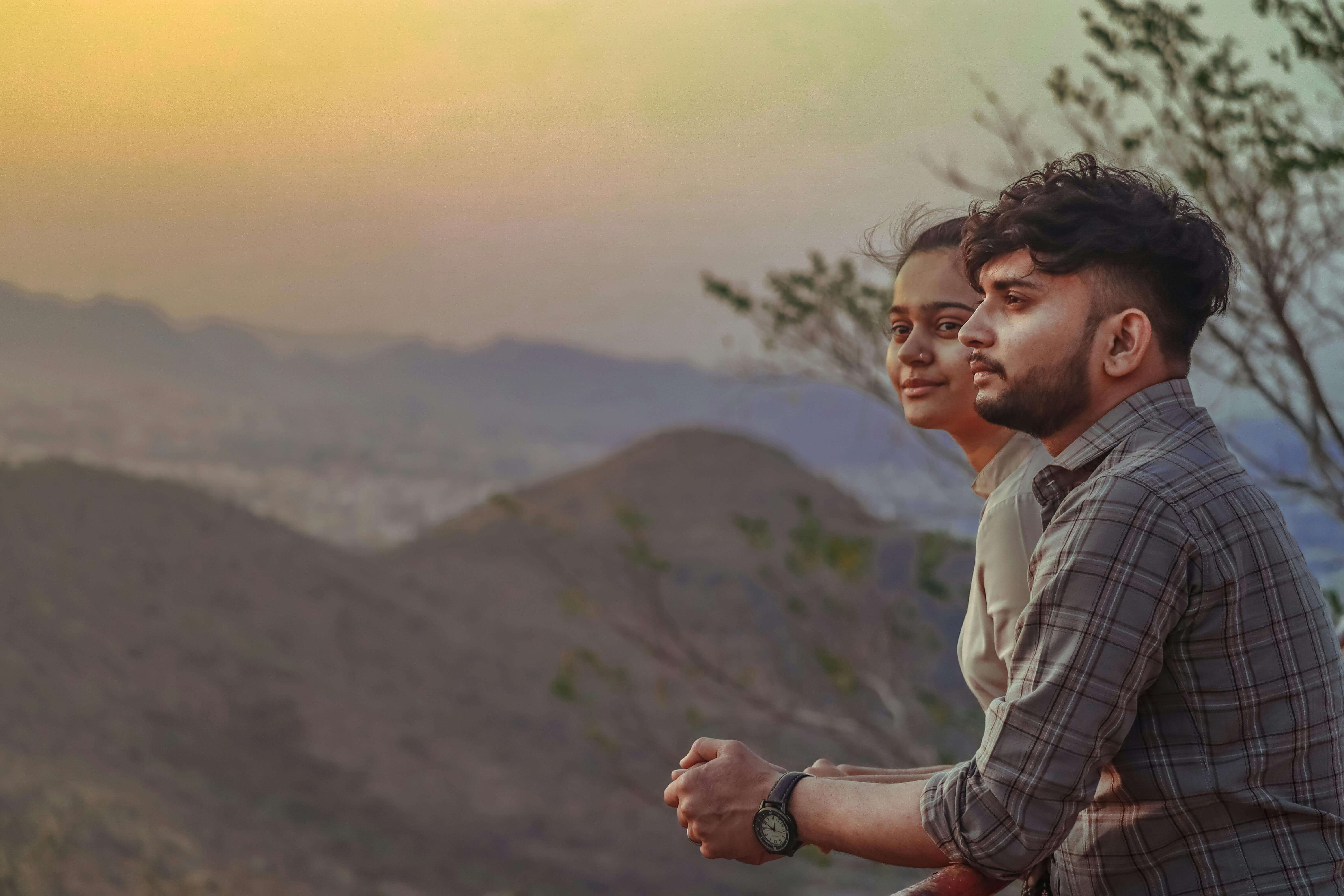 A couple enjoys a serene mountain view during sunset, creating a peaceful moment in nature.