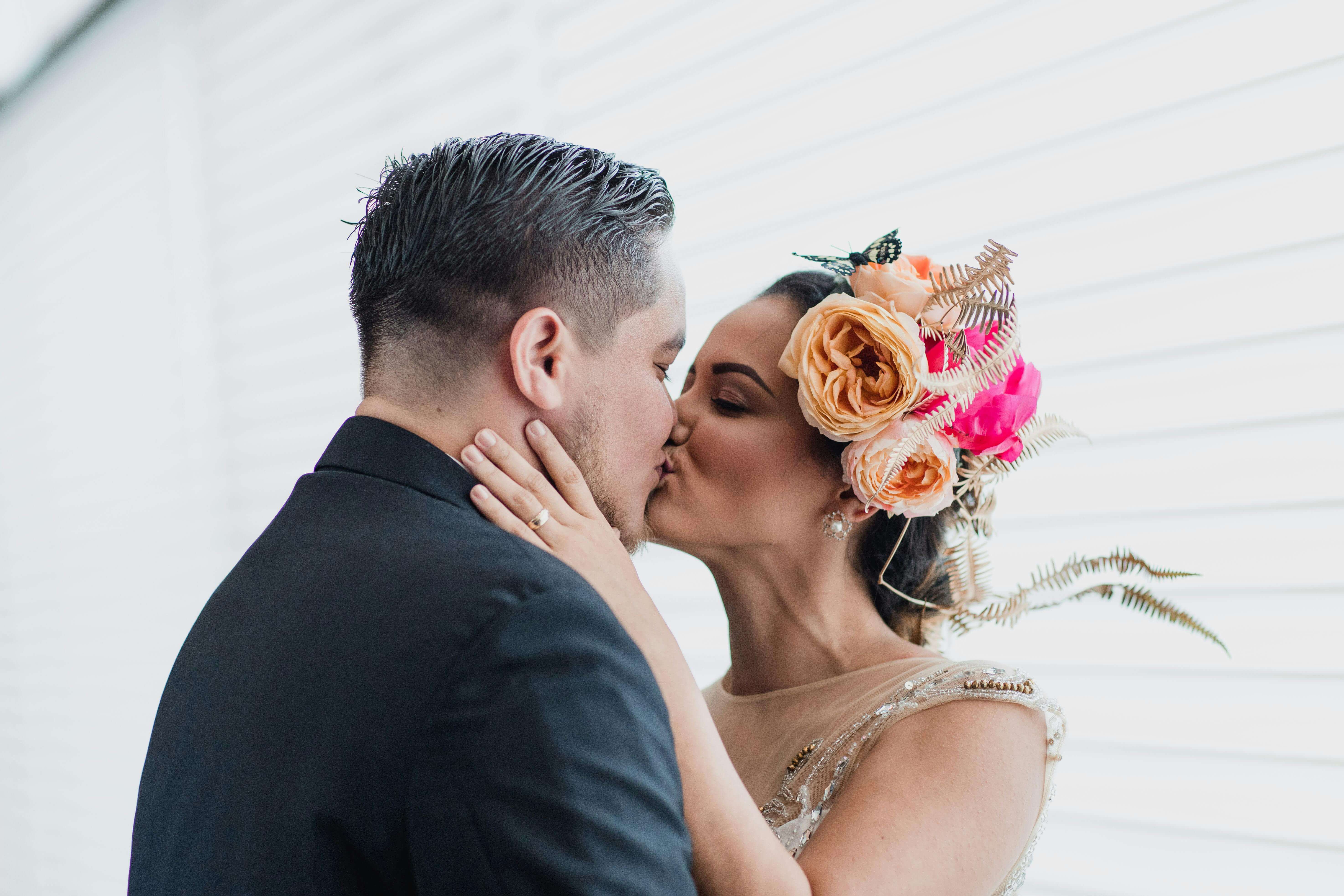 Elegant wedding couple sharing intimate kiss with beautiful floral headpiece.