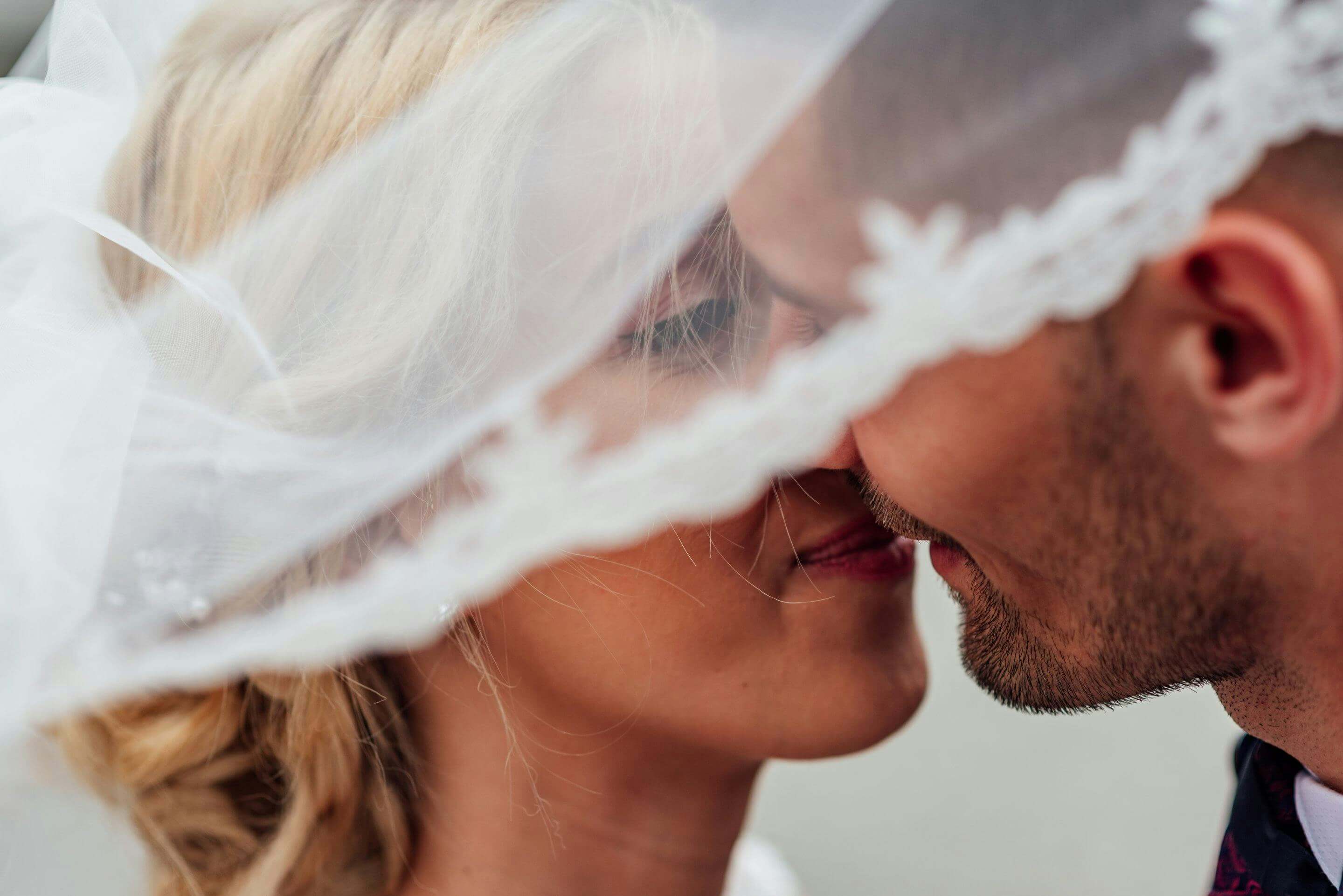 A close-up shot of a bride and groom embracing under a wedding veil symbolizing love.