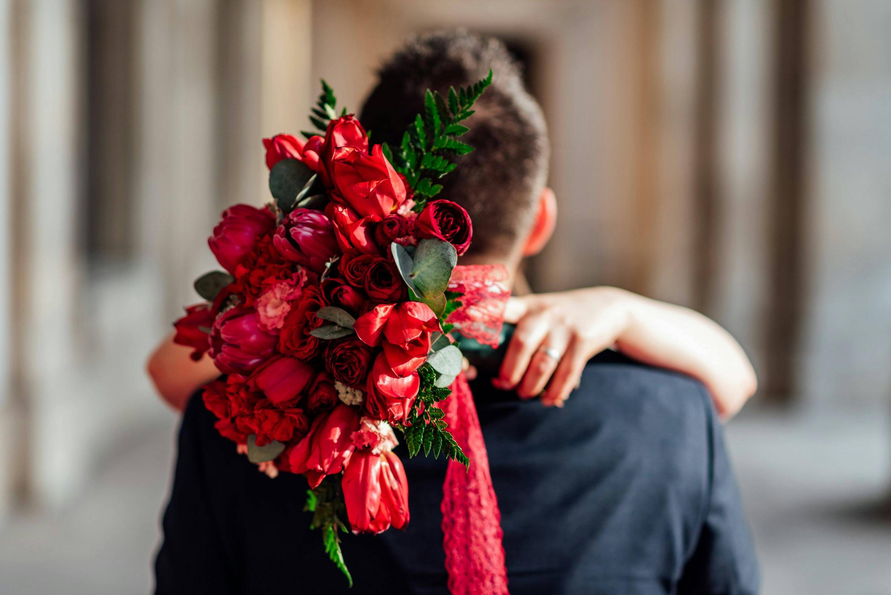 A couple embraces with a stunning bouquet of red roses in an elegant wedding setting.