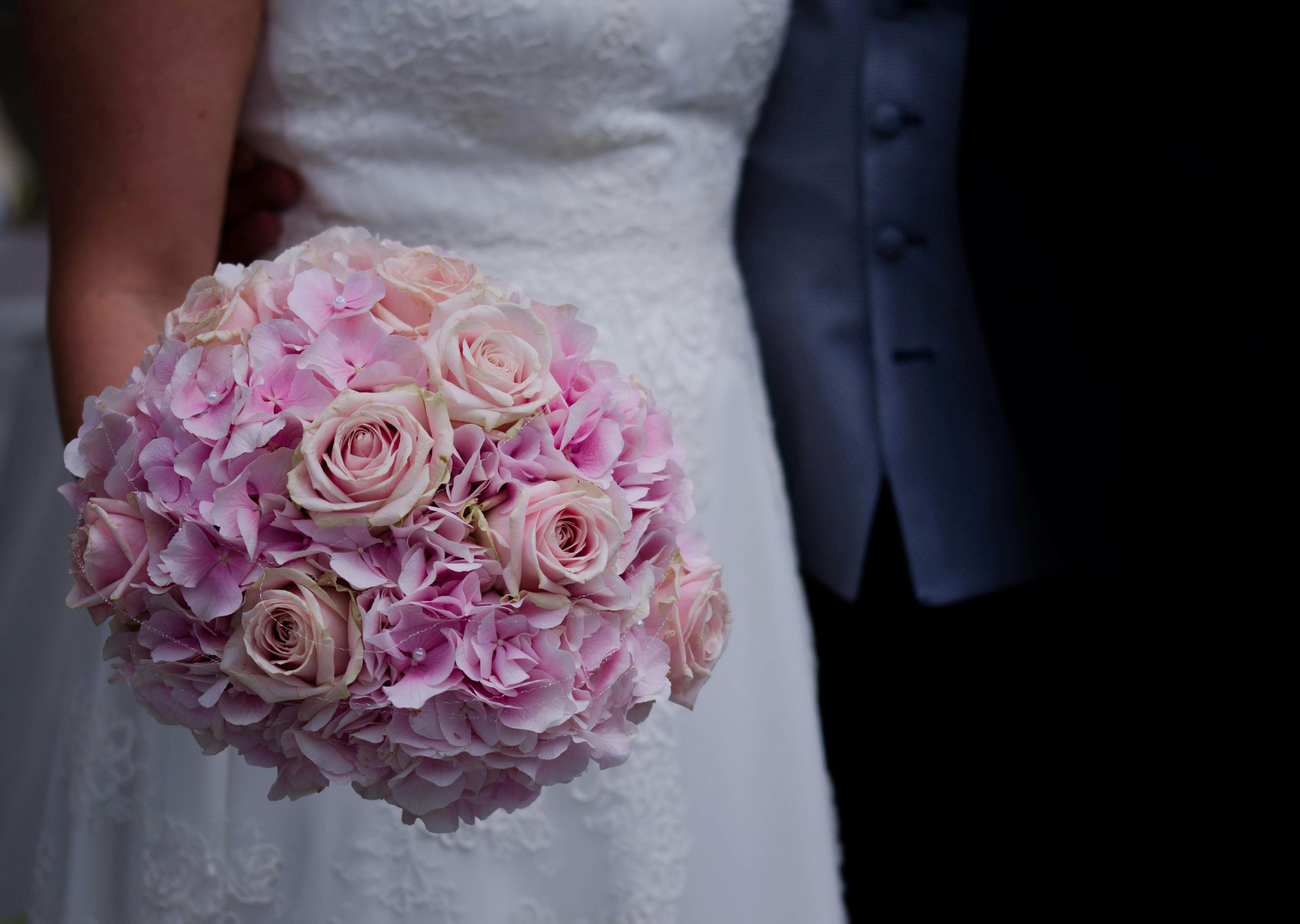 Close-up of a bride holding a bouquet of pink roses and hydrangeas, highlighting elegance and romance.