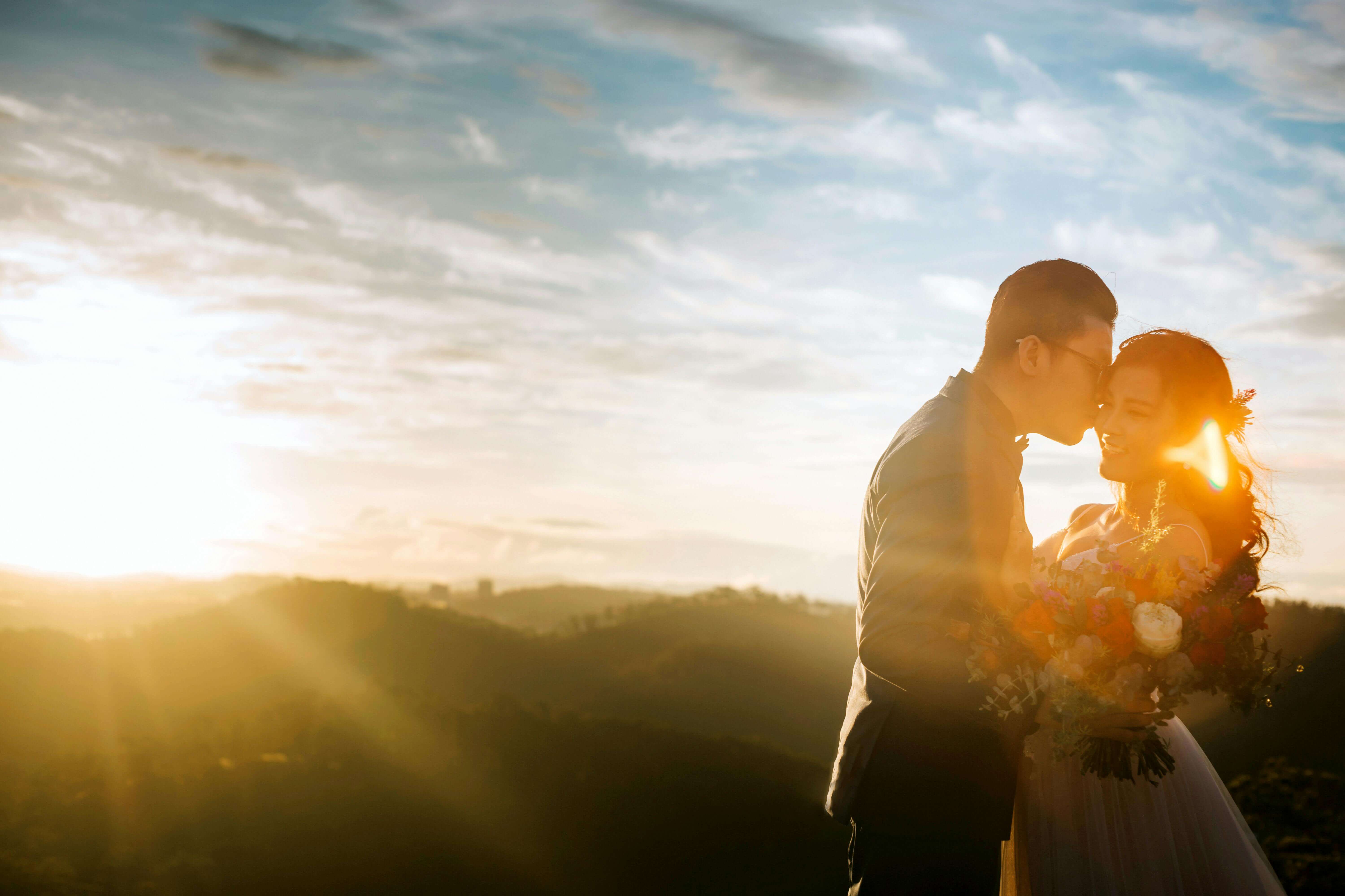 A romantic couple shares a tender moment with a stunning sunset and bouquet of flowers.