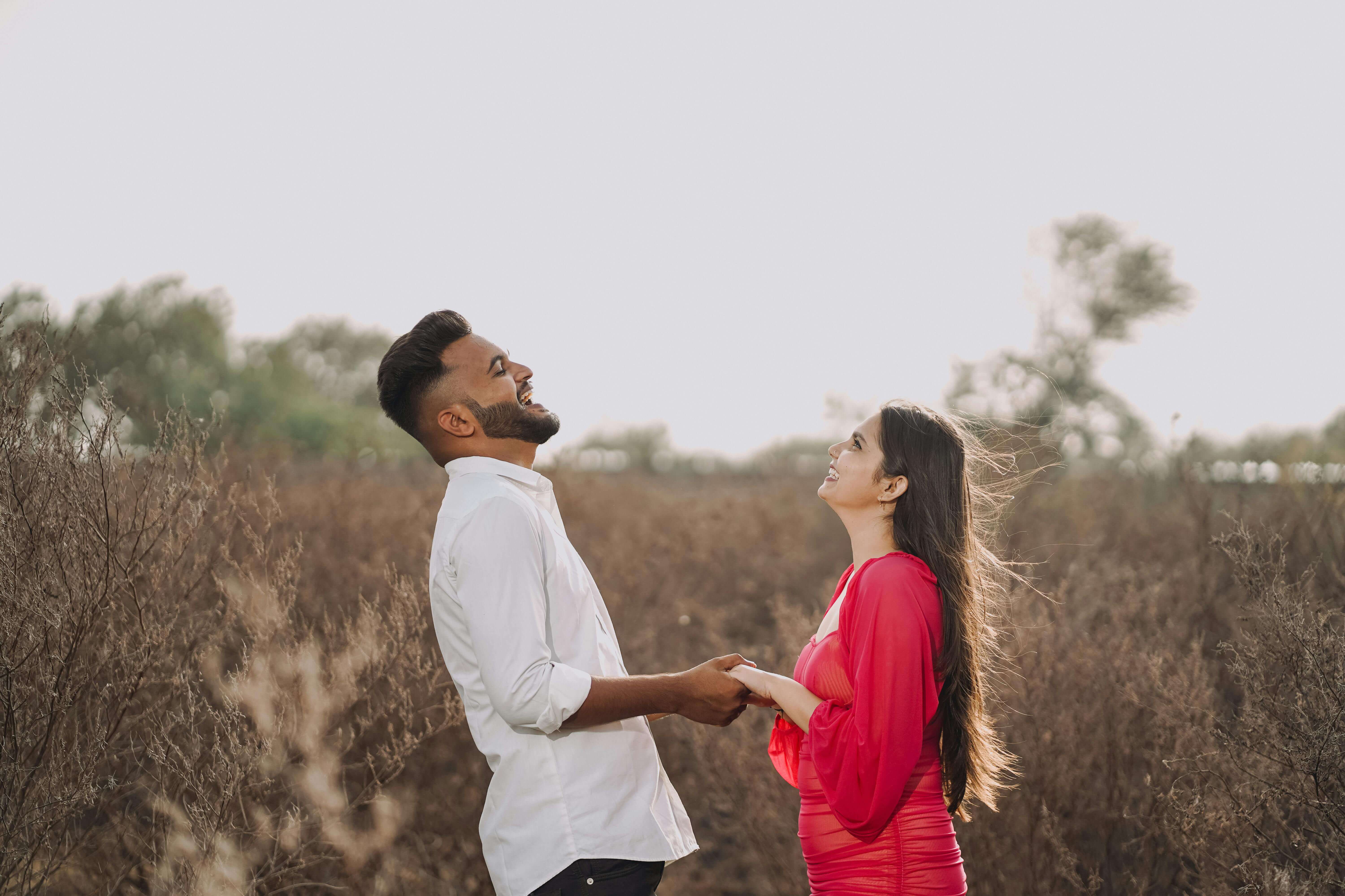 Joyful couple holding hands and laughing in a sunlit summer field.