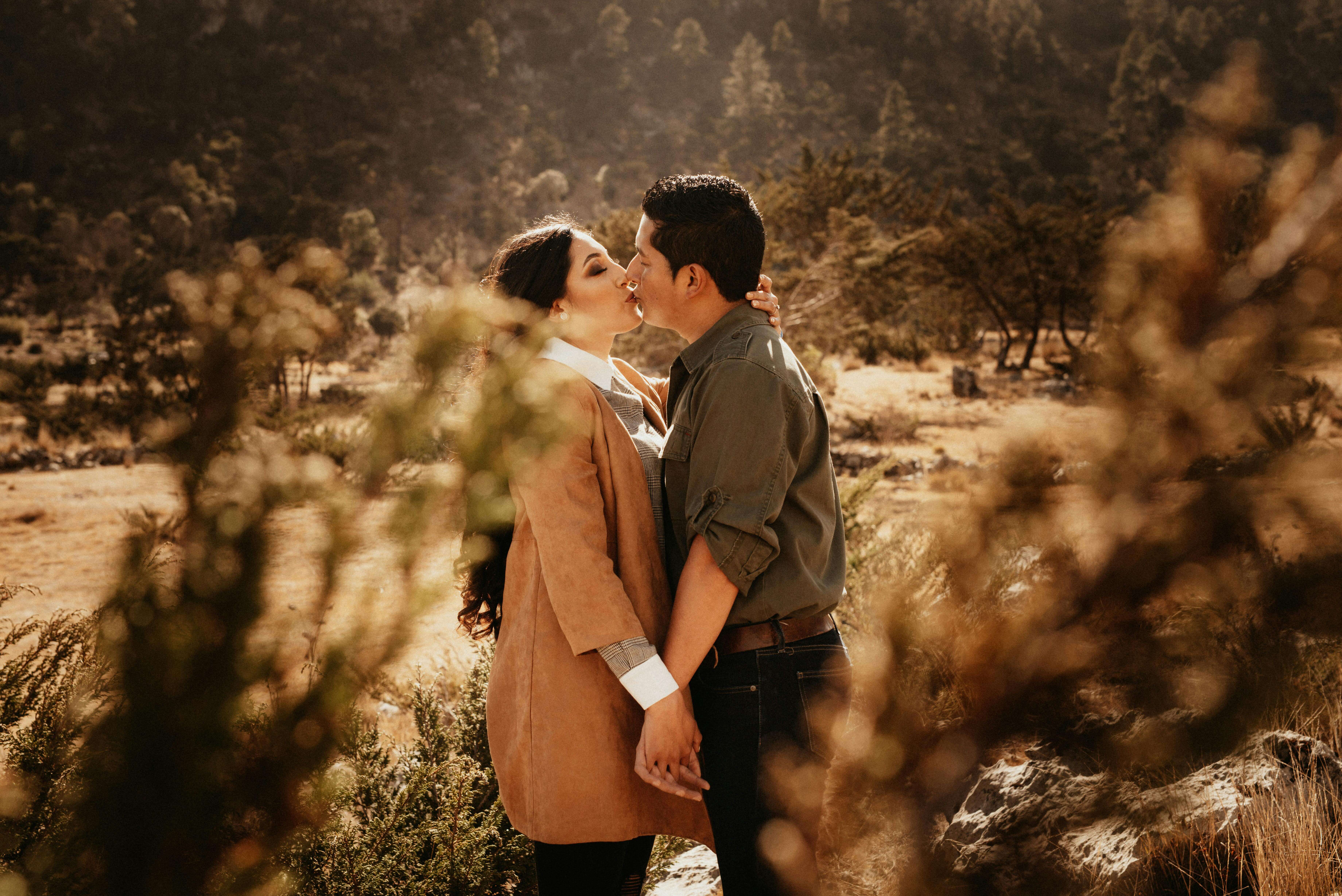 A loving couple shares a kiss while holding hands in a scenic autumn landscape.