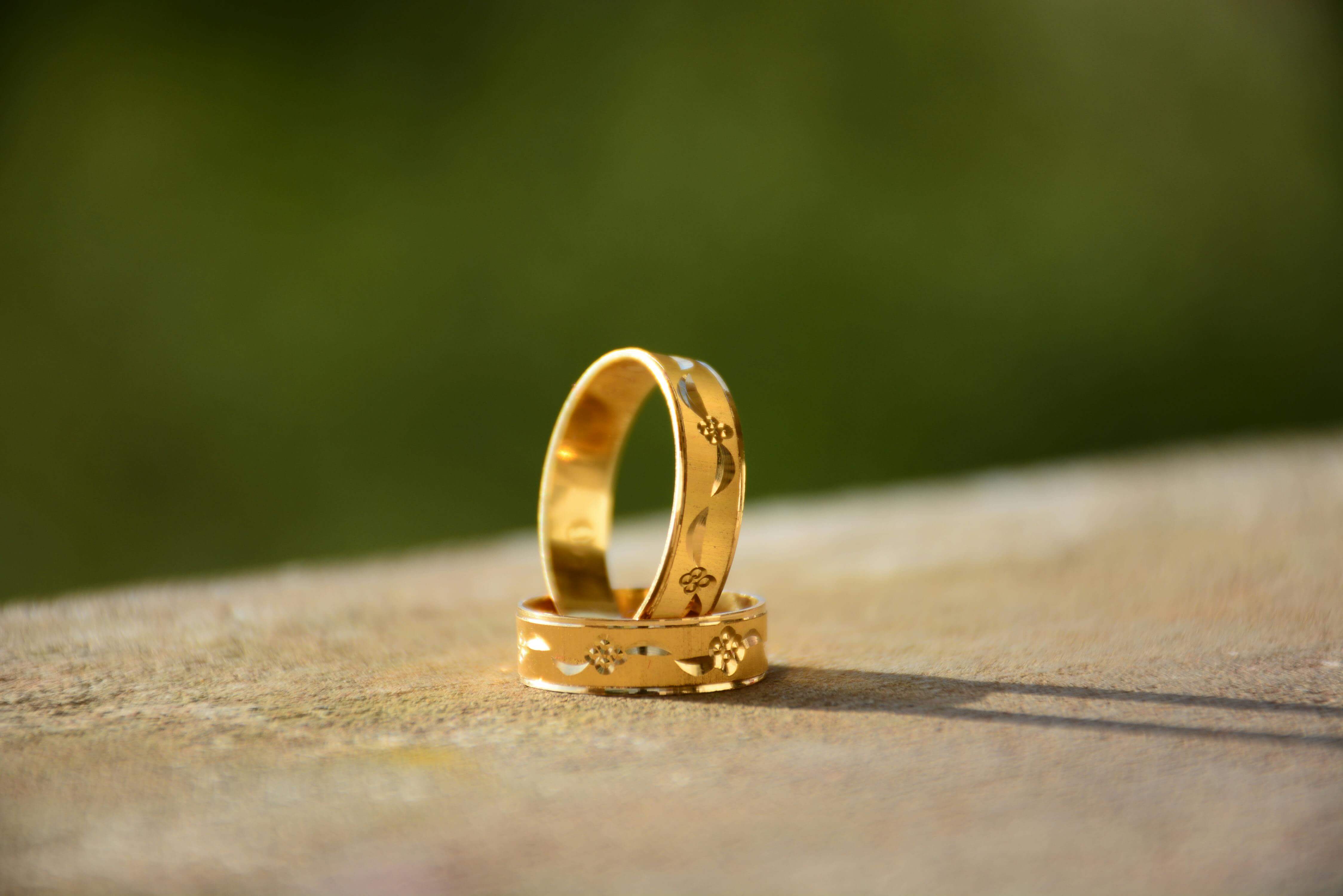 Close-up of two decorative gold wedding rings casting shadows on a warm surface.