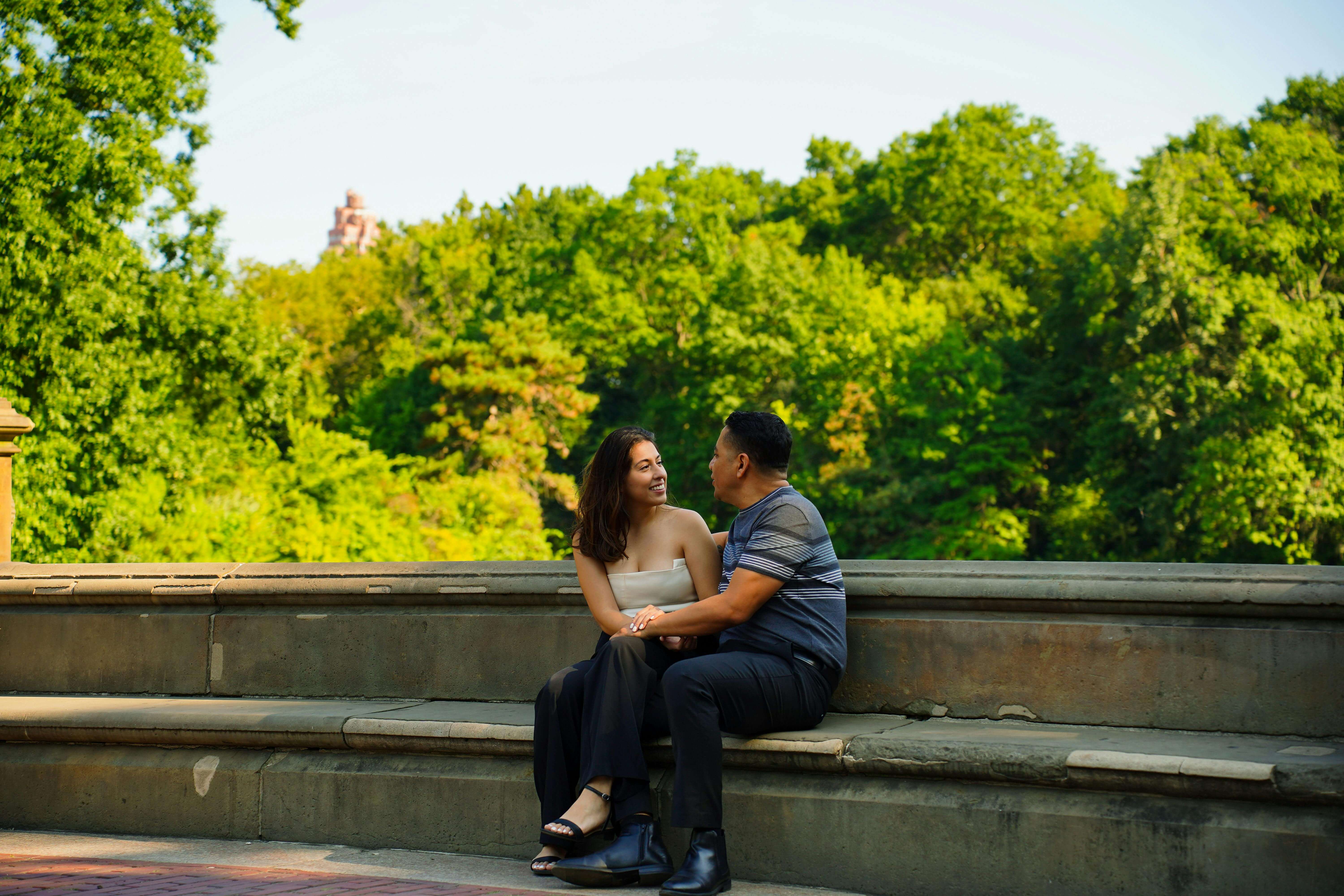 A couple sitting lovingly on a stone bench in Central Park, New York during summer.