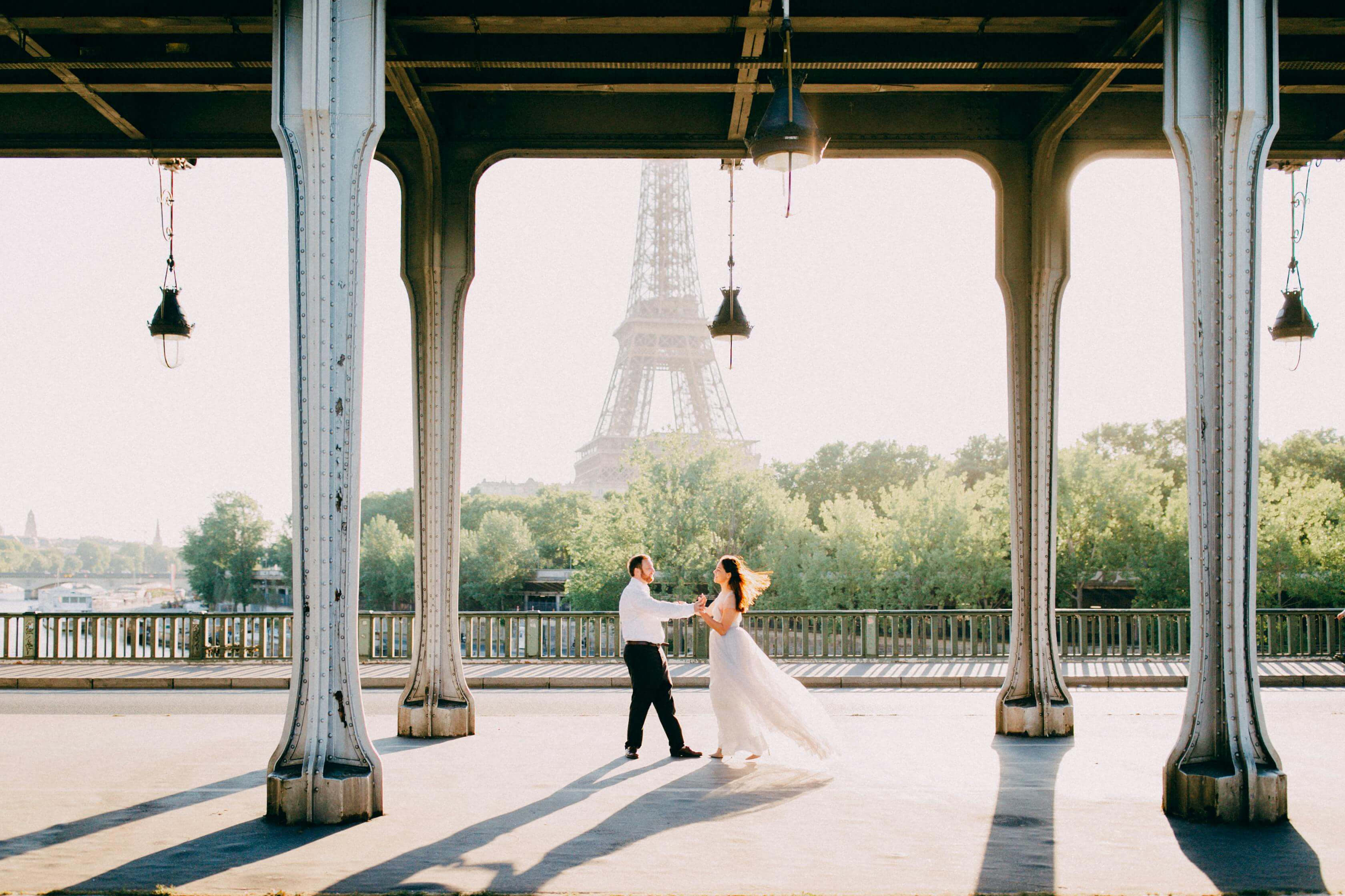 A couple dances under a bridge with the Eiffel Tower in the background in Paris.