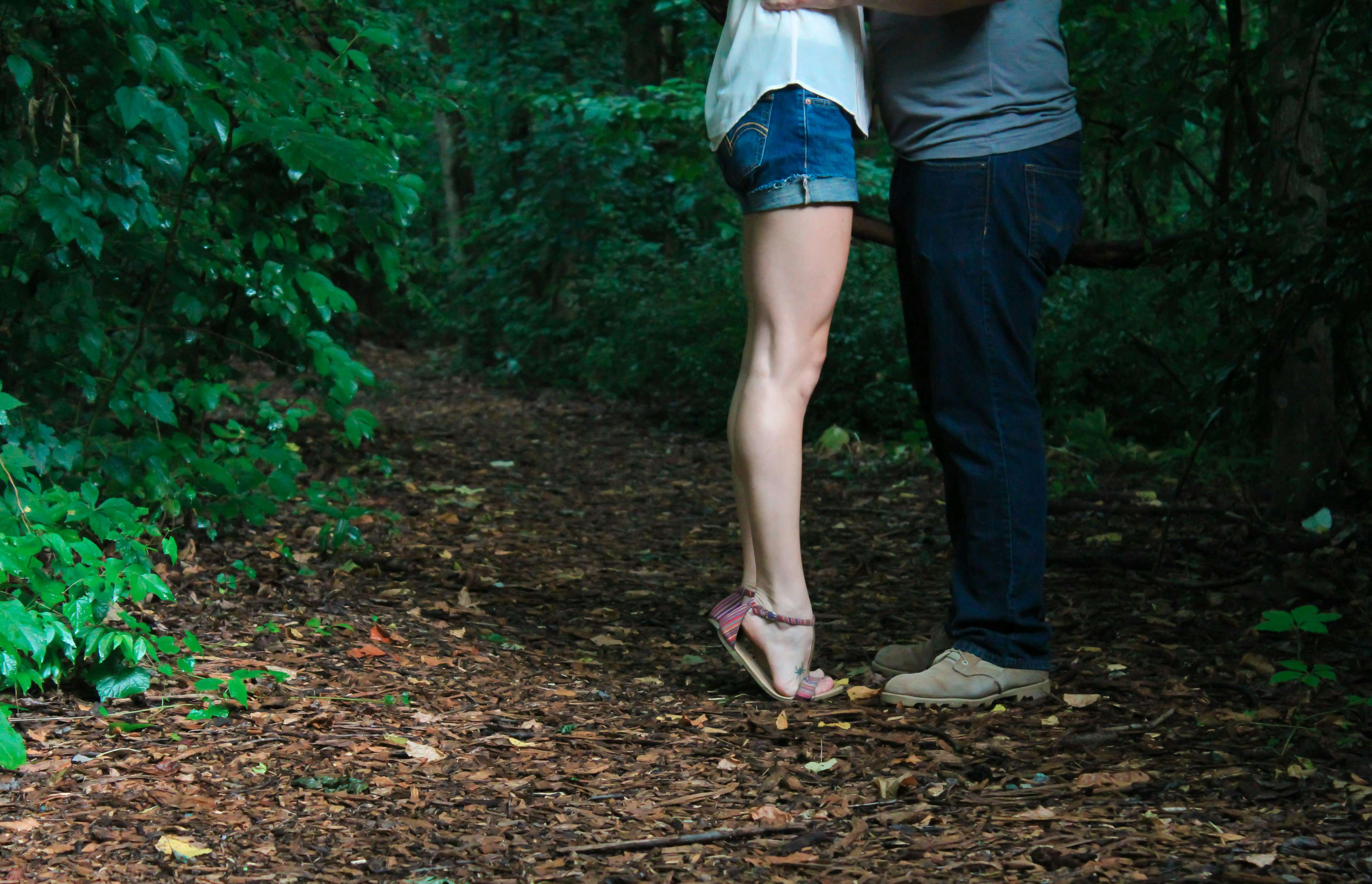 A loving couple embracing on a secluded forest pathway surrounded by lush greenery.
